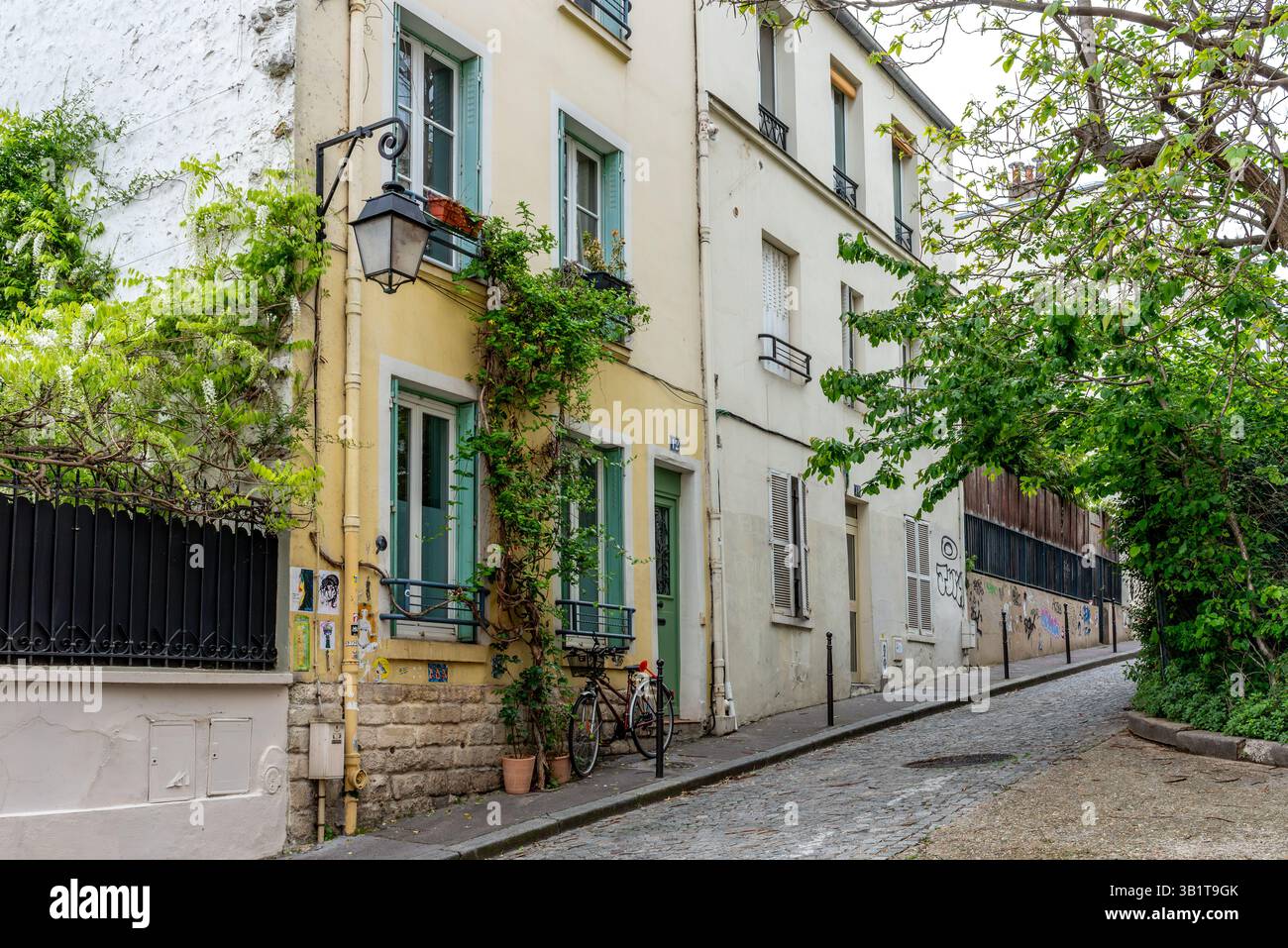 Eine charmante Kopfsteinpflasterstraße in La Butte aux Cailles im 13. Arrondissement von Paris. Ein gelbes Haus mit pastellgrünen Fensterläden, dörfliches Ambiente Stockfoto
