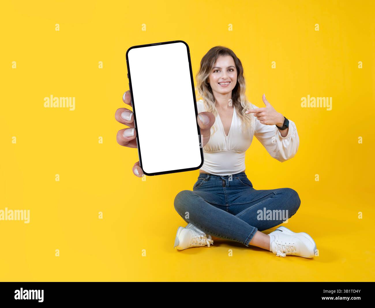 Wunderschönes weißes blondes Mädchen mit Zahnspangen, das einen großen, leeren Bildschirm des Mobiltelefons zeigt, stellt sich ganz nah vor der Kamera vor. Zeigender Touchscreen. Stockfoto