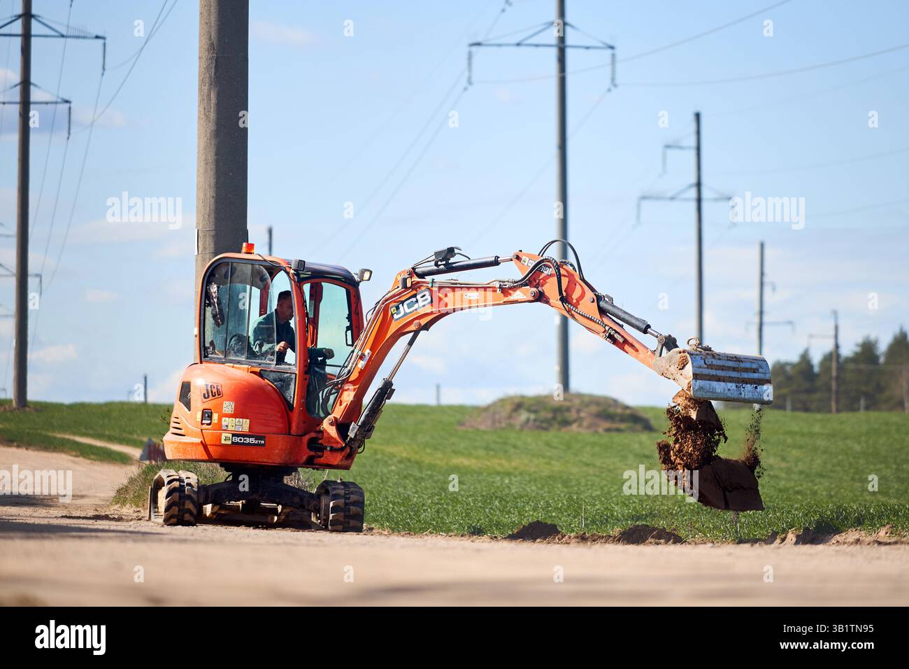 Mir, Weißrussland - 7. April 2025: JCB 8035 ZTS Minibagger mit Arbeiter im Grabboden auf dem Feld. Graben für Kabel oder Rohrleitungen. Stockfoto