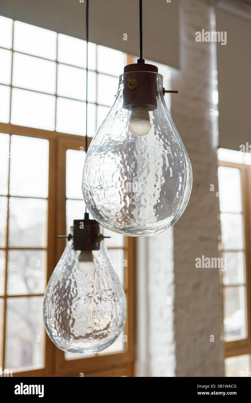 Zwei dekorative Lampen, Kronleuchter aus strukturiertem Glas im Loft-Wohnzimmer auf großem Fensterhintergrund. Innenarchitektur, Beleuchtung, Beleuchtung Stockfoto