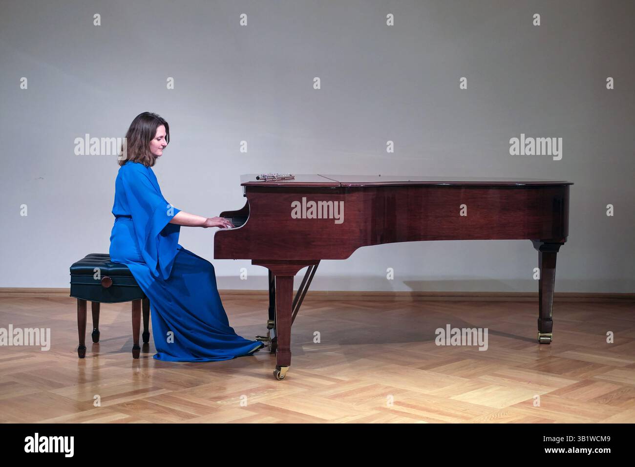 Die Frau spielt elegant auf einem Flügel in einer ruhigen Umgebung, in einem fließenden blauen Kleid. Ihr fokussierter Ausdruck unterstreicht die emotionale Tiefe und Stockfoto