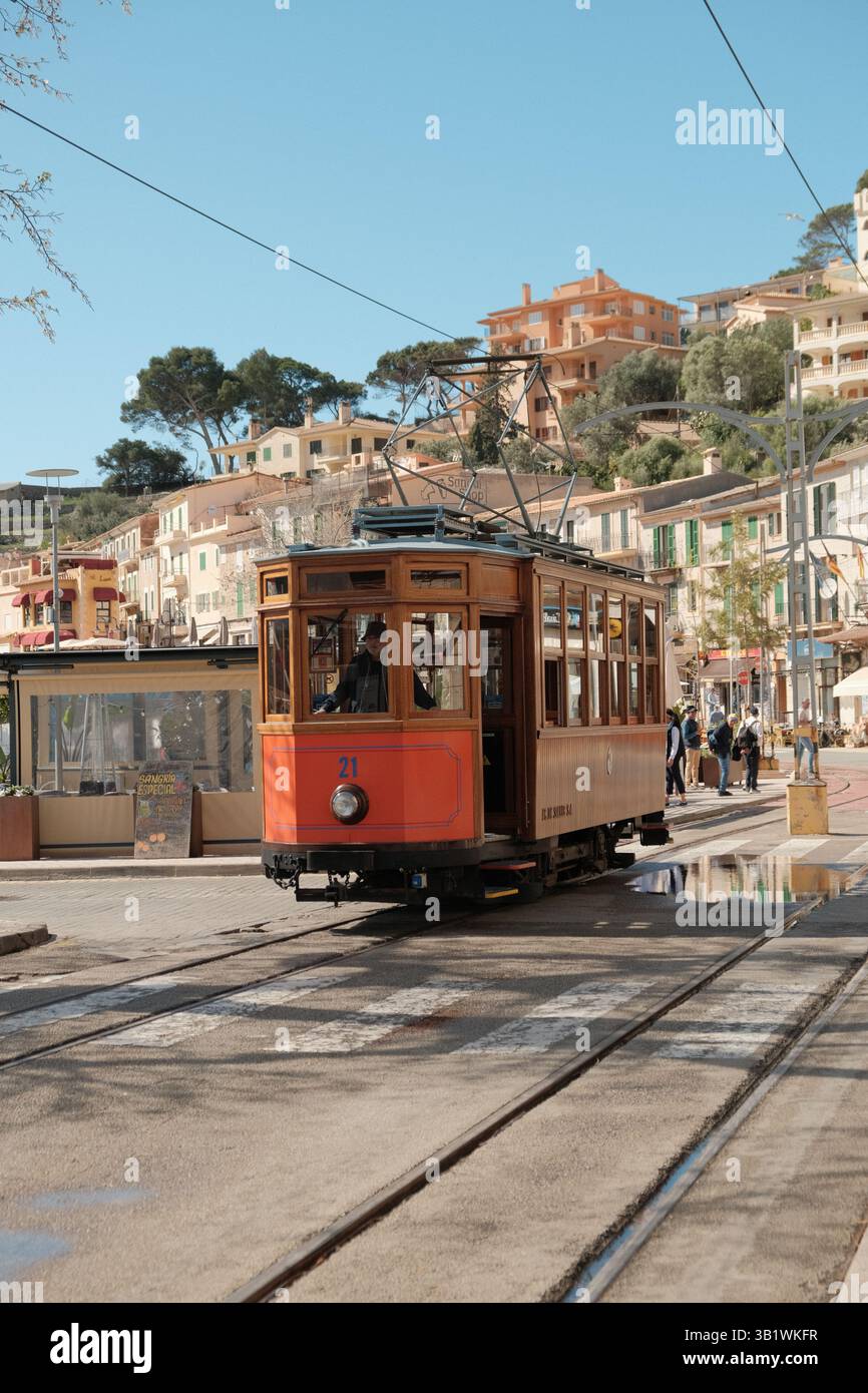 Traditionelle rote Straßenbahn, die durch eine malerische Straße mit historischen Gebäuden auf einem Hügel in einer mediterranen Stadt auf Mallorca fährt. Stockfoto