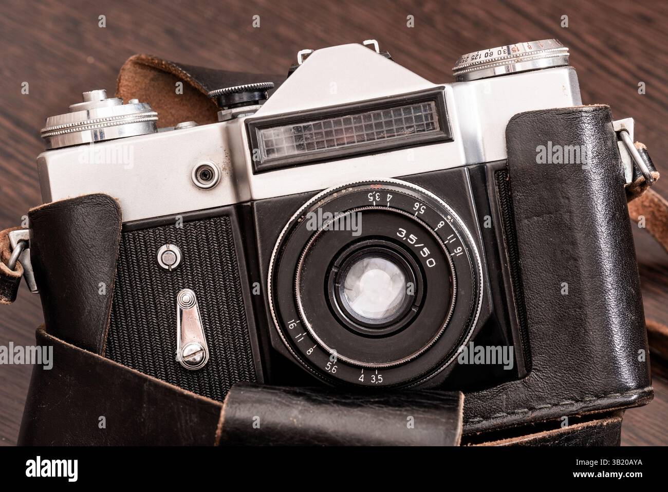 Die Classic Vintage Old Shabby Fotokamera in einem dunkelbraunen Gehäuse mit offenem Objektiv aus braunem Naturleder, Holztisch mit Bügel Stockfoto