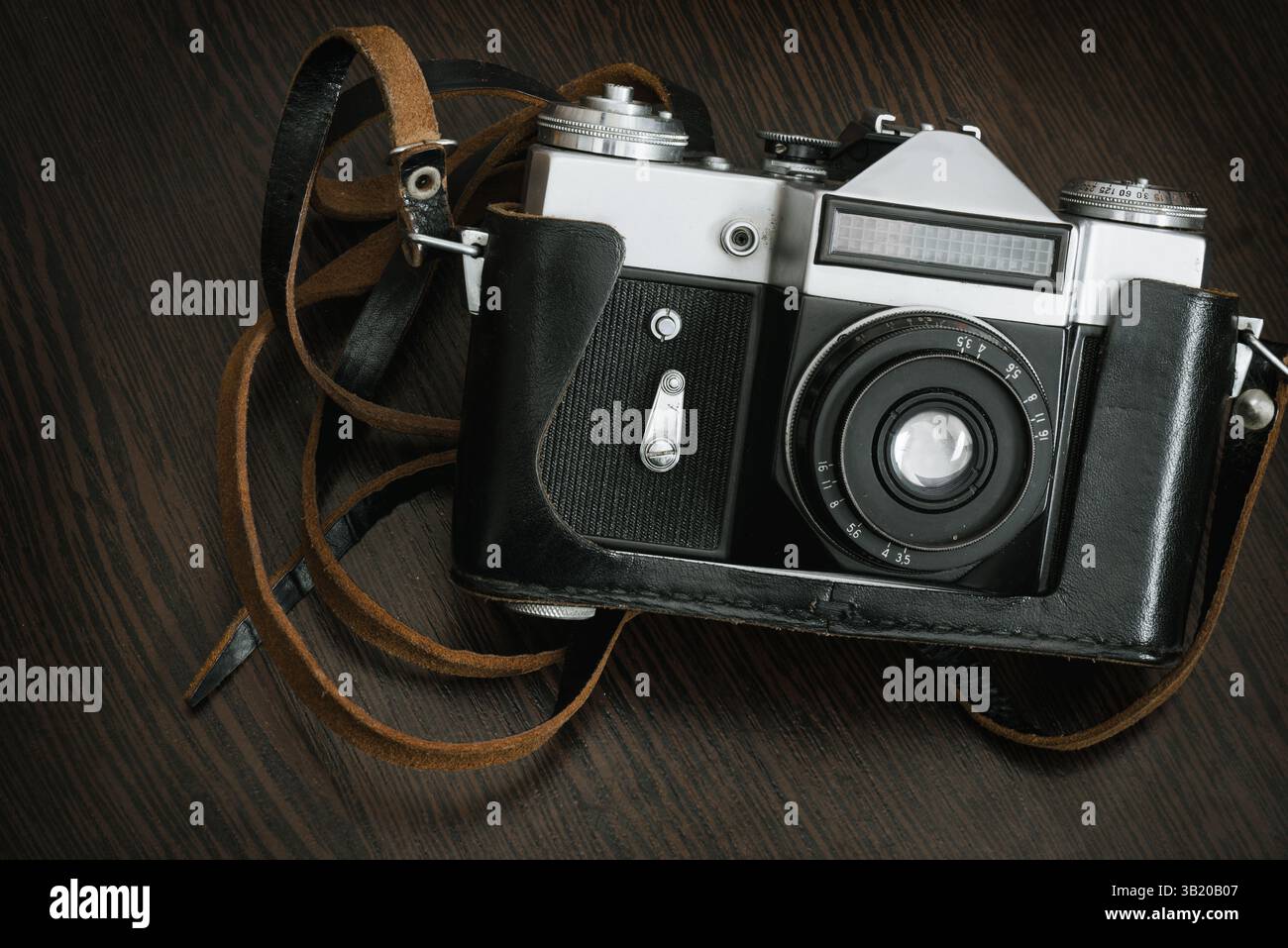 Die Classic Vintage Old Shabby Fotokamera in einem schwarzen Gehäuse mit offener Linse braunes Naturlederband auf Holztischhintergrund Stockfoto