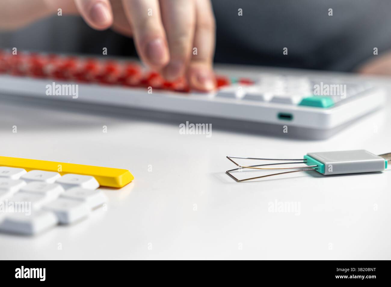 Nahaufnahme einer Person, die eine mechanische Tastatur mit einem Tastenkappenzieher und Ersatztastenkappen modifiziert, um ein DIY-Setup zu zeigen, das sich auf die individuelle Anpassung konzentriert Stockfoto
