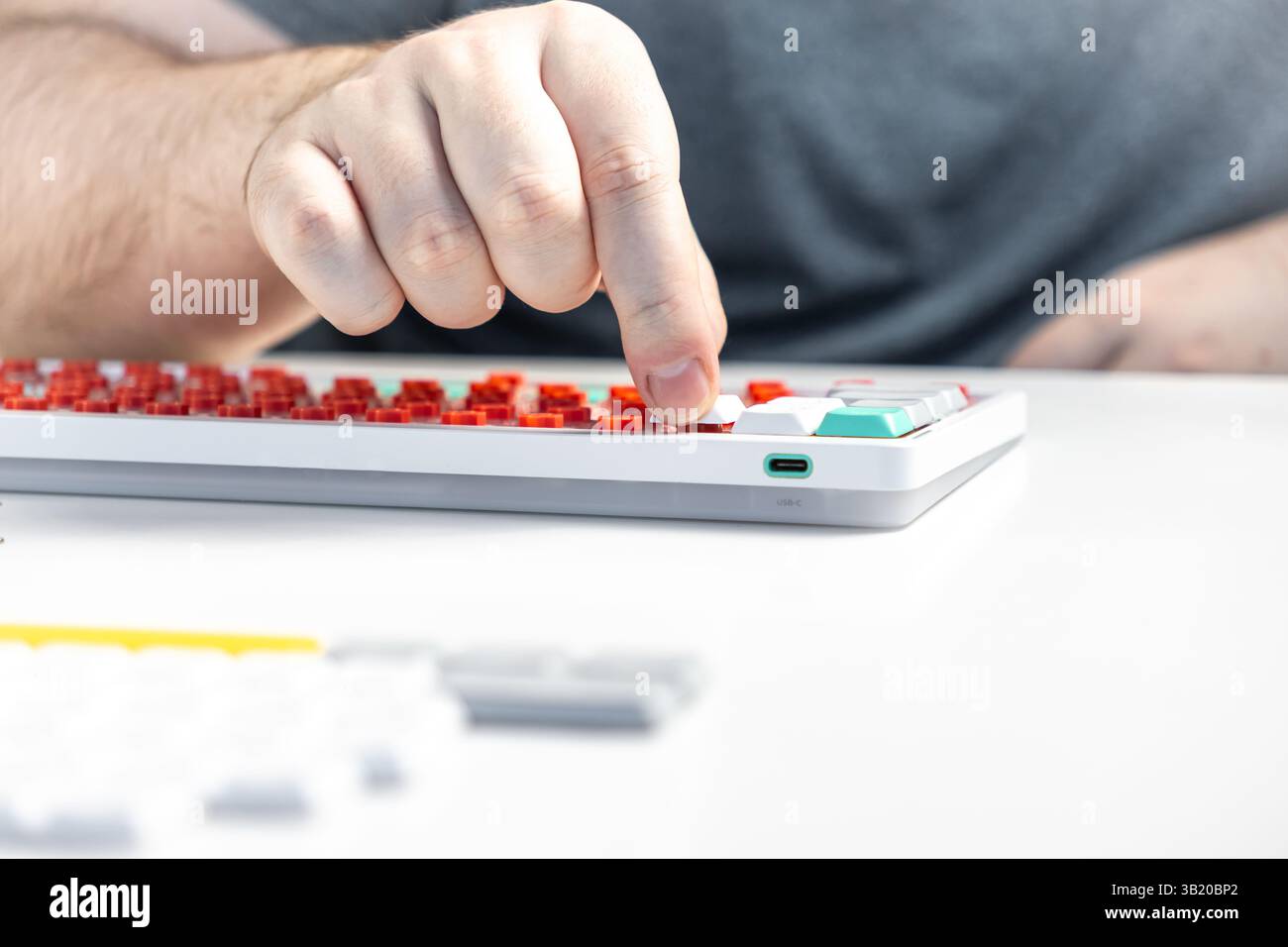 Nahaufnahme einer Person, die eine Tastenkappe auf einer mechanischen Tastatur mit roten Schaltern installiert, wobei die praktische Anpassung, die ergonomische Einrichtung und die persönliche Bedienung hervorgehoben werden Stockfoto