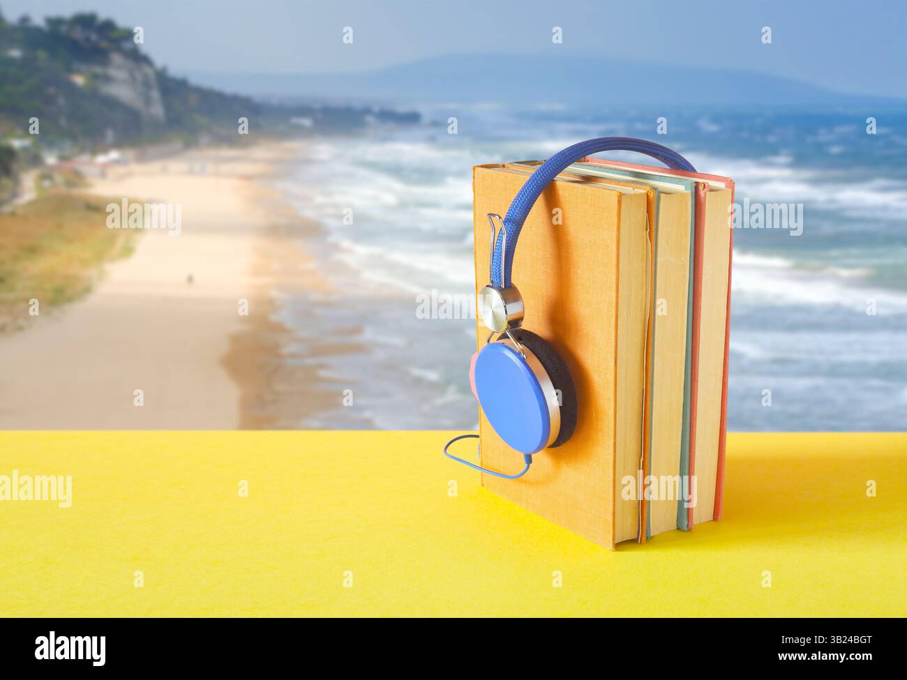 Hörbuch mit Bücherreihe und Vintage-Kopfhörer. Entspannend mit Hörbüchern während des Urlaubs, wunderschöne Meereslandschaft hinten. Stockfoto