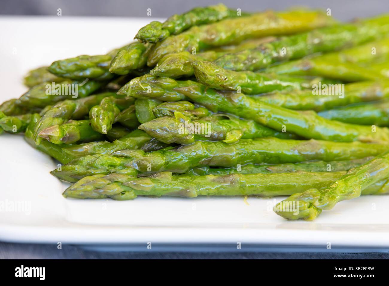 Gekochter grüner Spargel in Butter auf einer weißen Platte Stockfoto