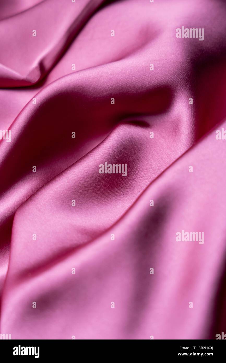 Ein weiches, hellrosafarbenes Tuch, das sanft mit einer glatten Textur und einem subtilen Glanz fließt, perfekt für eine elegante Atmosphäre Stockfoto