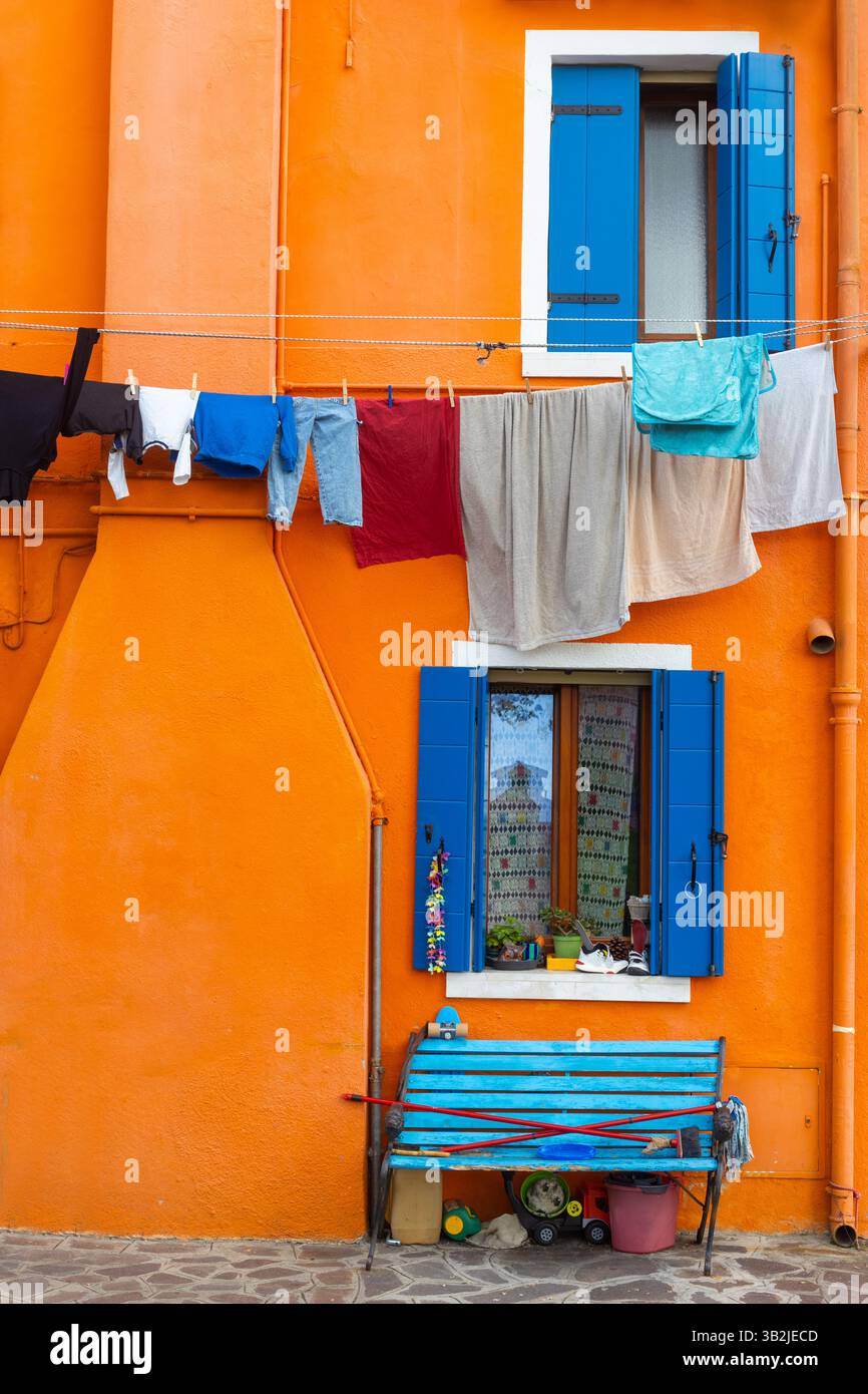 Farbenfrohe orangefarbene Wand mit blauen Fensterläden und Wäscherei in Burano Italien Stockfoto