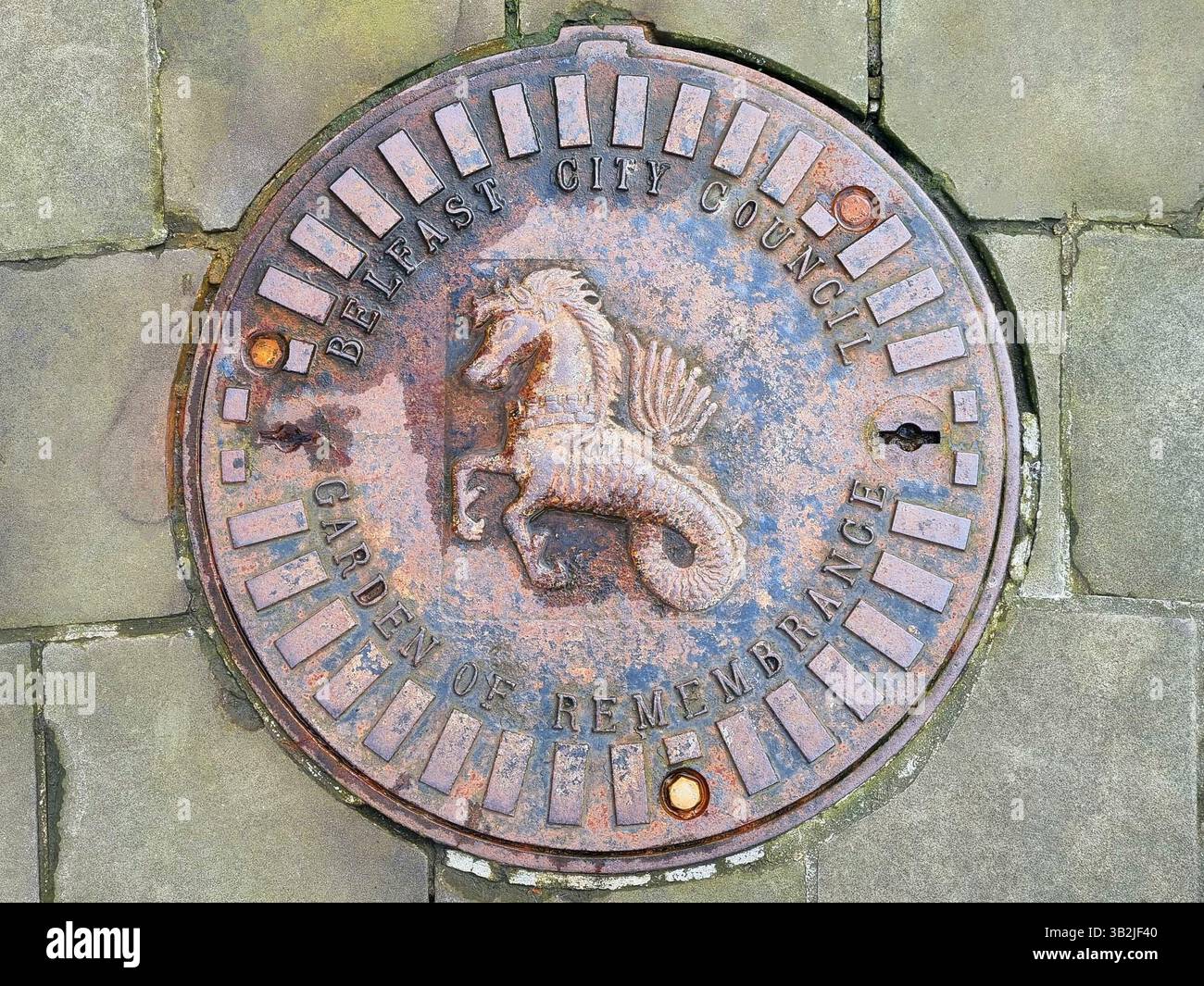 Einzigartige dekorative gusseiserne Mannlochabdeckung mit Reliefbild eines Seepferdes aus dem Wappen von Belfast, Nordirland Stockfoto