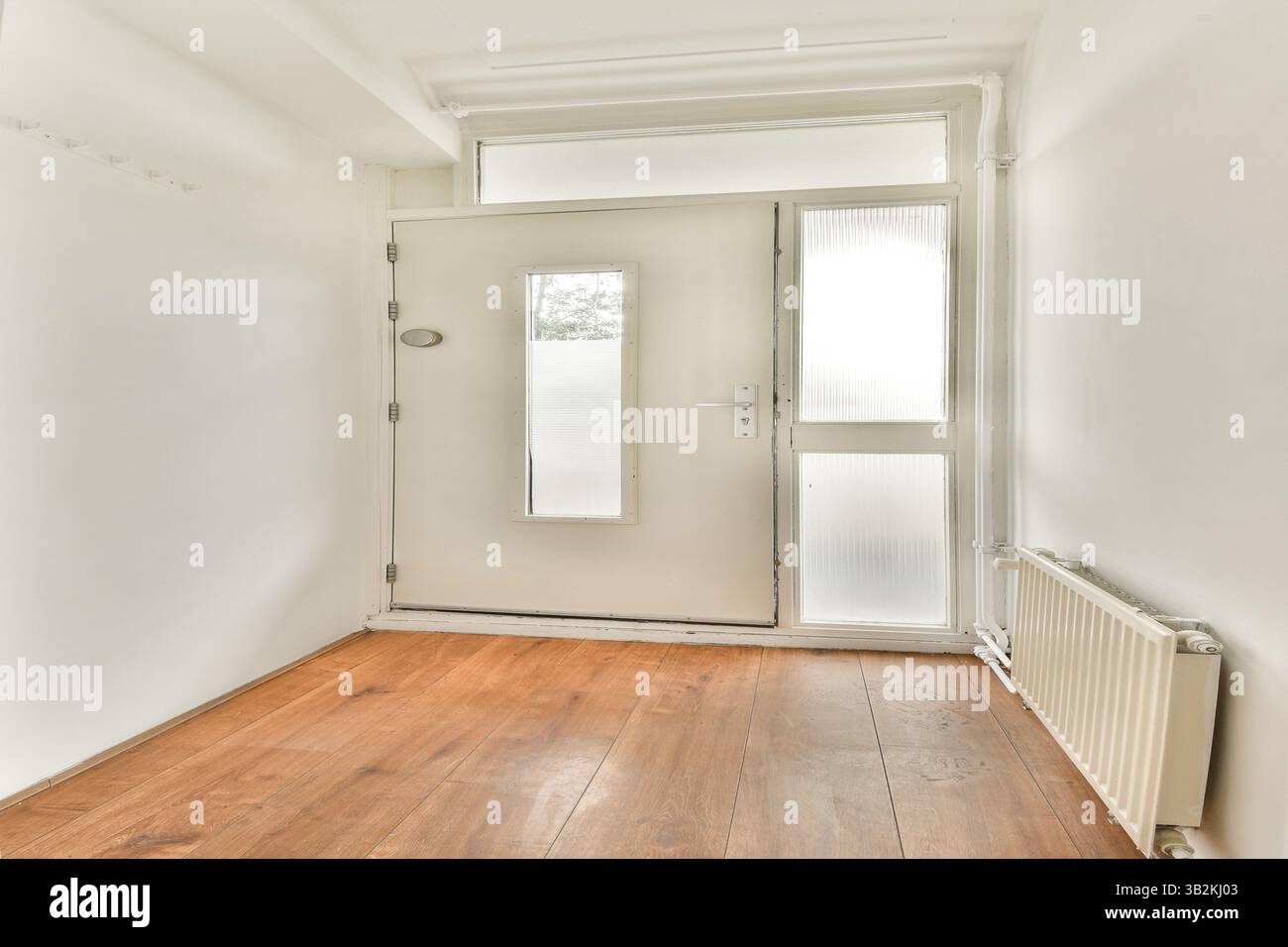 Eine helle und saubere Eingangshalle mit neutralen Wänden, natürlichem Holzfußboden und einer großen Glastür schafft ein einladendes Ambiente. Stockfoto