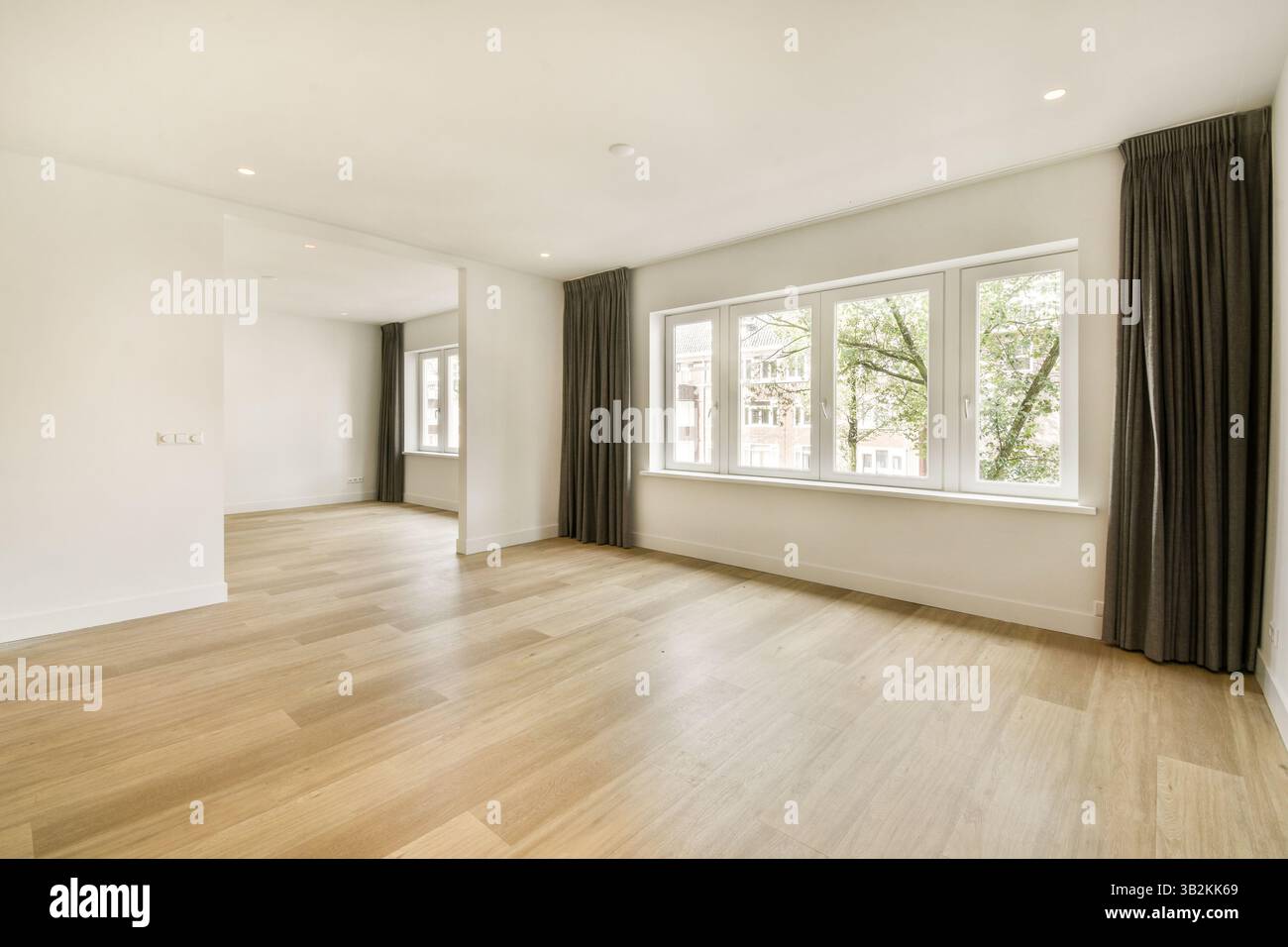 Ein heller und luftiger Innenraum mit großen Fenstern und minimalistischem Design. Der Boden ist aus Holz und die Wände sind in einem sanften, neutralen Ton gestrichen. Stockfoto