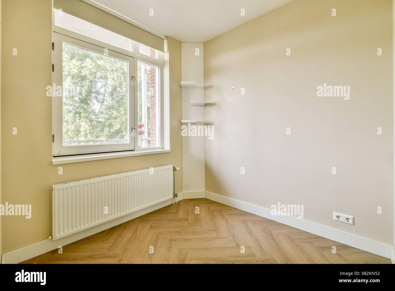 Die dezent beleuchtete, minimalistische Inneneinrichtung mit einer Ecke mit Fenster, glatten Wänden und hellem Holzfußboden sorgt für ein einladendes Ambiente. Stockfoto