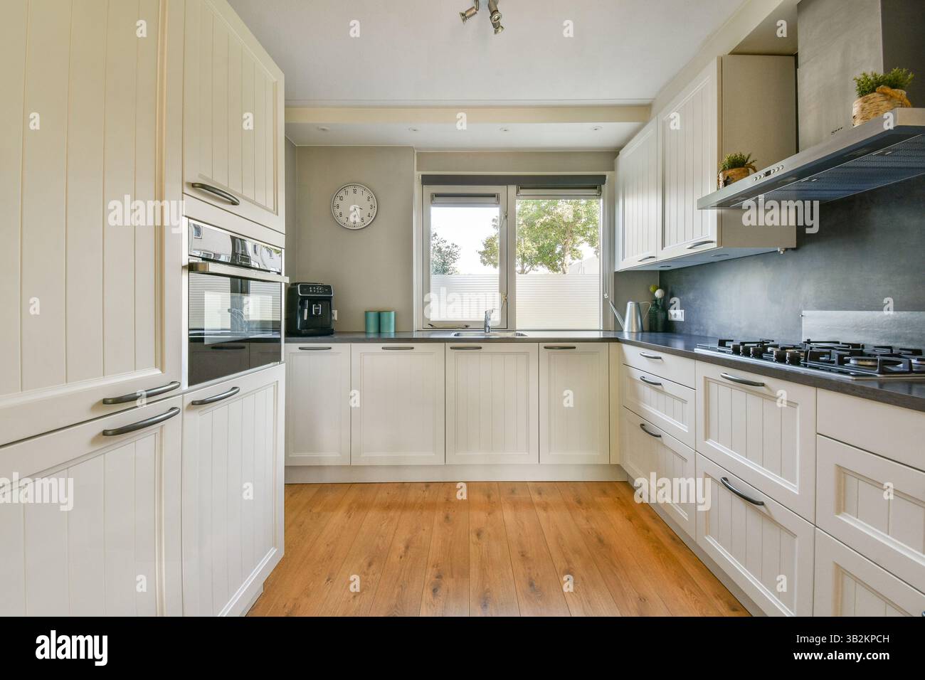 Eine stilvolle, moderne Küche mit weißen Schränken, Holzböden und eleganten Geräten bietet eine helle und geräumige Atmosphäre zum Kochen und Essen. Stockfoto