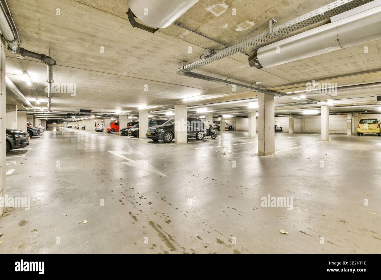 Eine weitläufige Tiefgarage mit zahlreichen geparkten Autos, Betonwänden und Deckenbeleuchtung bietet viel Platz für Fahrzeuge. Stockfoto