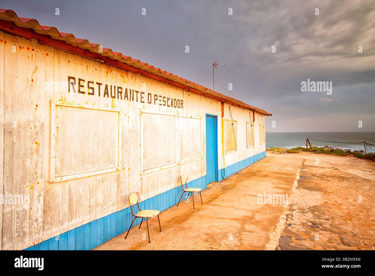 Dunkler Schiefer Sonnenuntergang über der Küste von Almograve an der Küste von Alentejo. Portugal. Altes verlassenes Restaurant Stockfoto