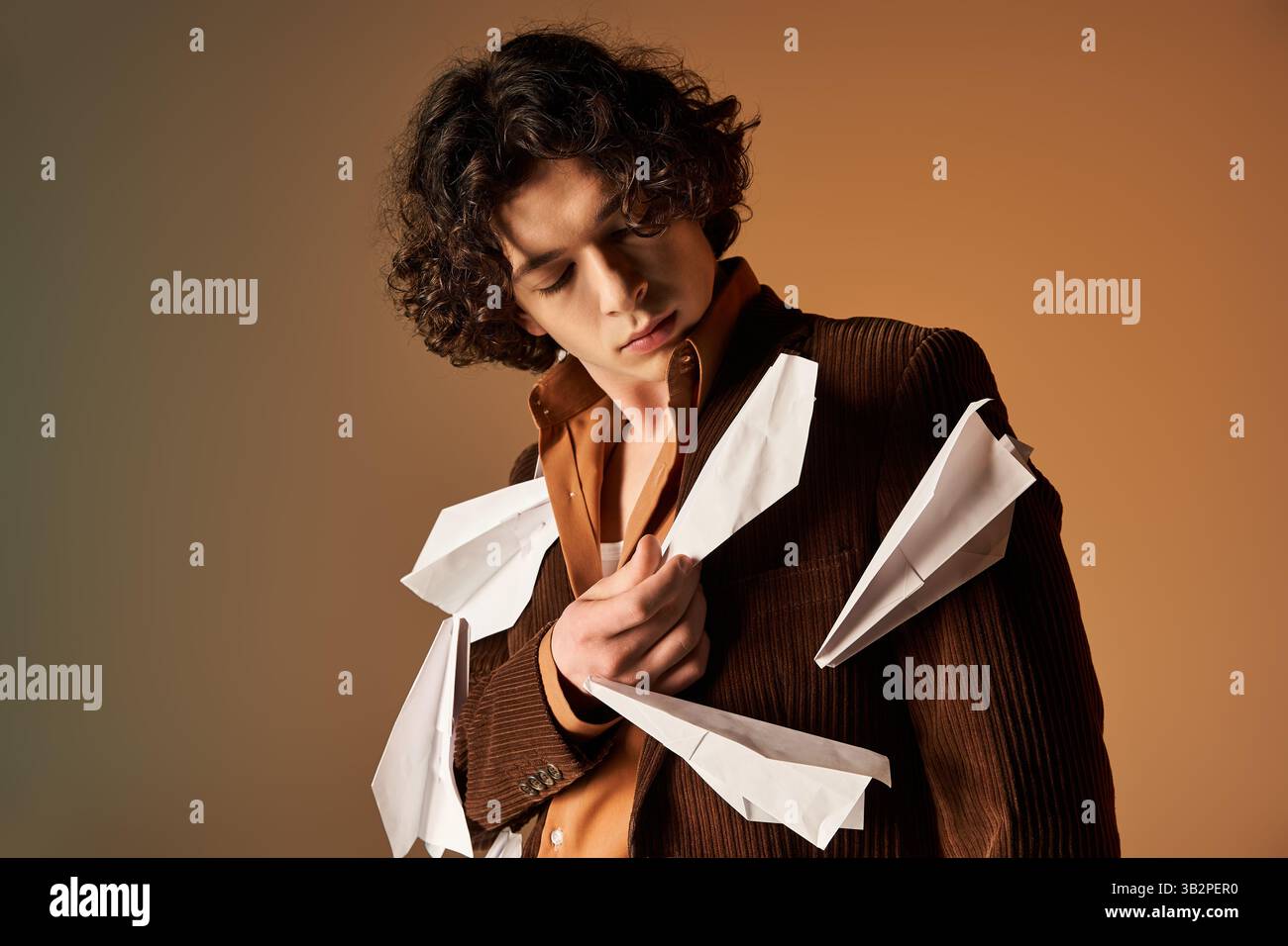 Ein junger Mann verströmt Charme in einem braunen Cordblazer mit verspielten Papierflugzeugen. Stockfoto