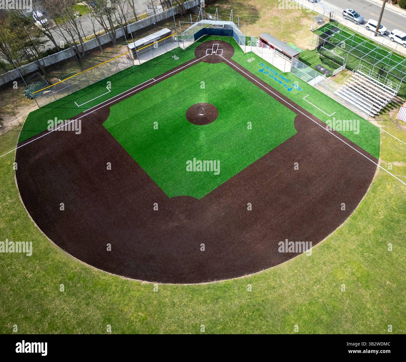 Blick auf ein Baseballfeld im Frühling mit lebhaftem grünen Rasen, leeren Bachern und einem Außenfeld mit Gras. Stockfoto