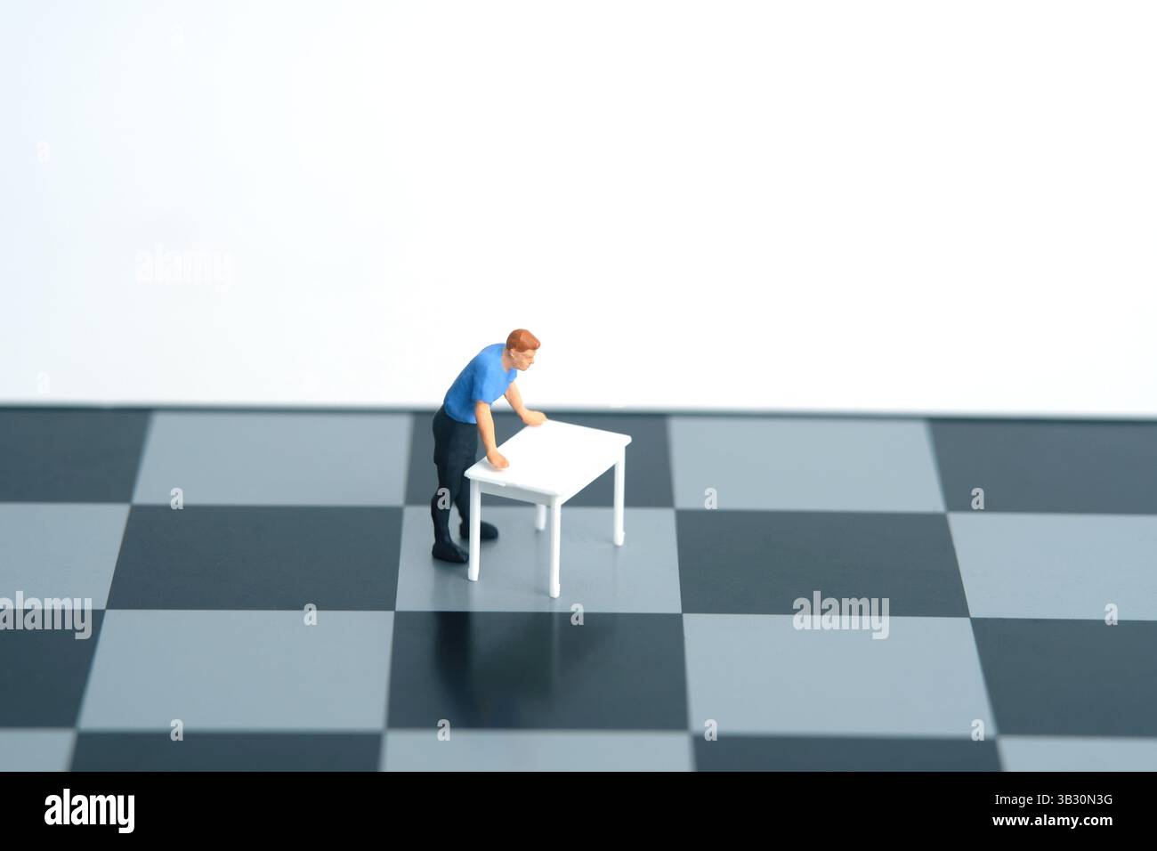 Ein Mann auf einem weißen Schreibtisch, der über dem Schachbrett einen strategischen Plan denkt. Miniatur Tiny People Spielzeug Fotografie. Isoliert auf weißem Hintergrund. Bild Foto Stockfoto