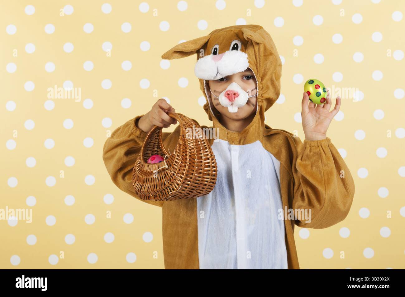 Kind verkleidet als Ostern Hase mit Korb Eiern auf gelben gestrichelten Hintergrund Stockfoto