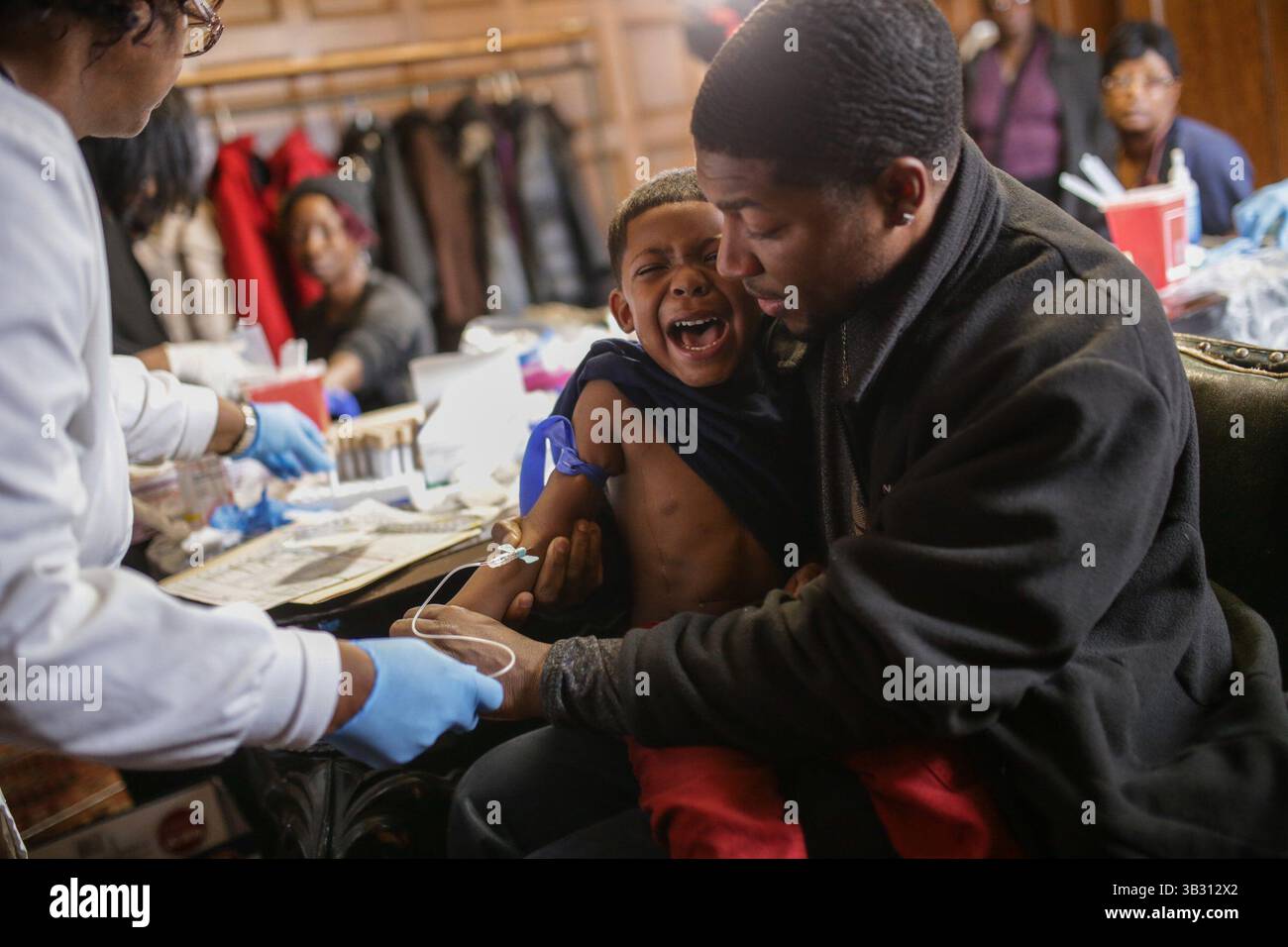 23. Januar 2016 - Flint, Michigan, USA - MIKE HENRY Sr. Aus Grand Blanc hält seinen Enkel KAIDEN OLIVARES, 3, während er eine Blutprobe gibt, die im Freimaurertempel in der Innenstadt von Flint auf Blei getestet werden soll. „Ich bin sauer, dass ich ihm das antun musste“, sagte Henry Sr., der mit seiner Familie außerhalb der Stadt nach Grand Blanc zog. Mein Enkel hatte Ausschläge. Er war im Krankenhaus. Wir haben jetzt Bedenken wegen des Krankenhauswassers. Meine Tochter hat in der Vergangenheit Haarausfall, dass wir keine Ahnung hatten. Wir versuchen nur herauszufinden, ob es vielleicht das war. Unsere ganze Familie wohnt in Flint. Wir haben in Flint gegessen. Stockfoto