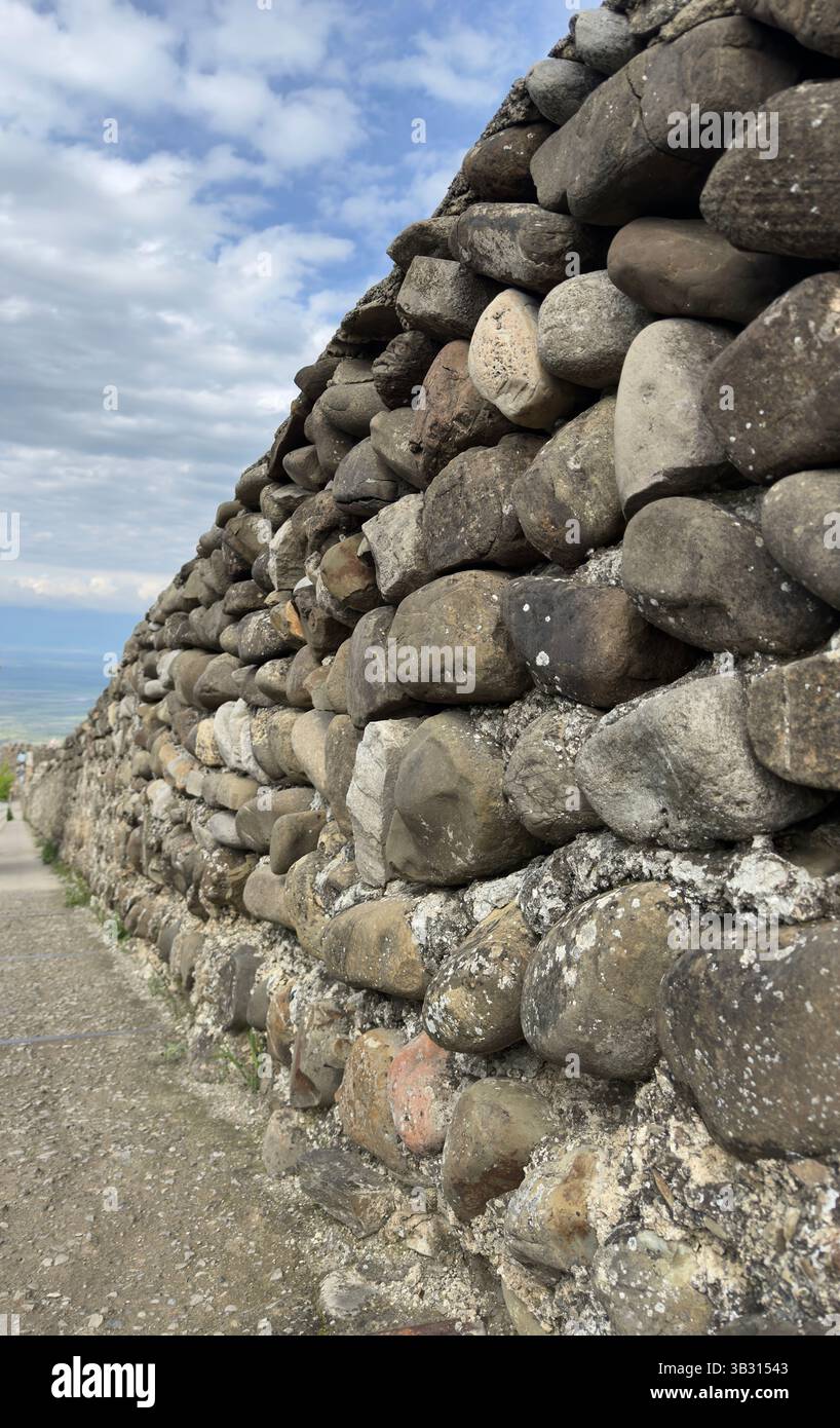 Verwitterte Steinmauer mit rauer Textur, bedeckt mit Moos und Flechten, Blick entlang der felsigen Wand. Perfekt für Architektur, Geschichte und Natur - Smartphone-aufgenommenes Stockfoto