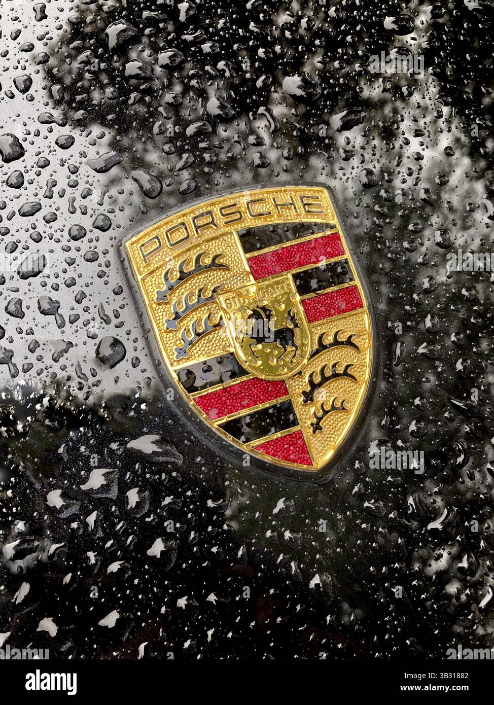 Porsche-Wappen auf schwarzer Motorhaube eines Sportwagens mit glitzernden Regentropfen, international Stockfoto