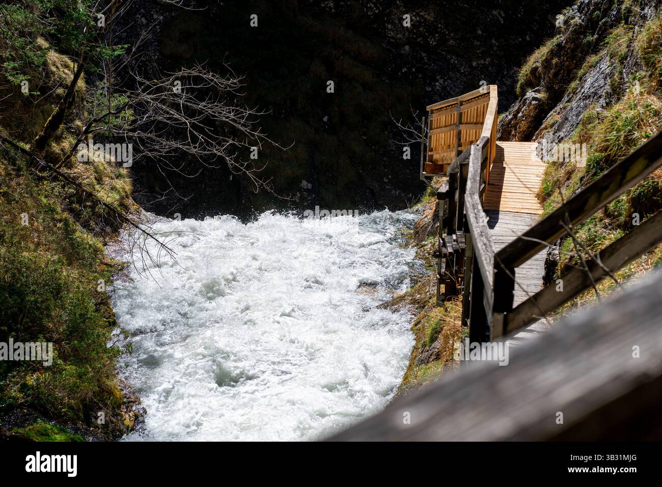 Eine hölzerne Hängebahn zwischen einem Berg und einem stürmischen Bergfluss Stockfoto