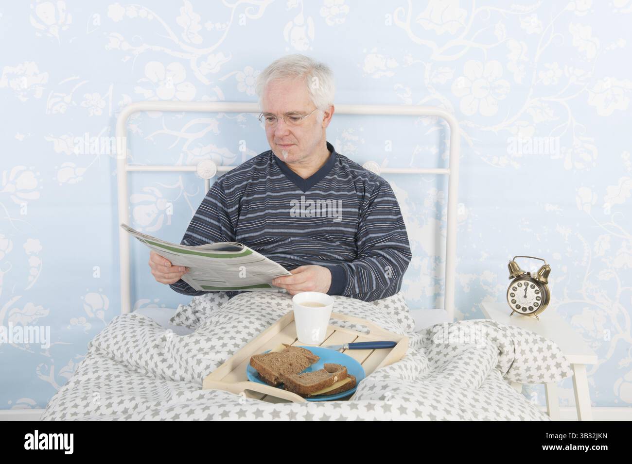 Mann liest Zeitungen weiß und frühstückt im Bett Stockfoto