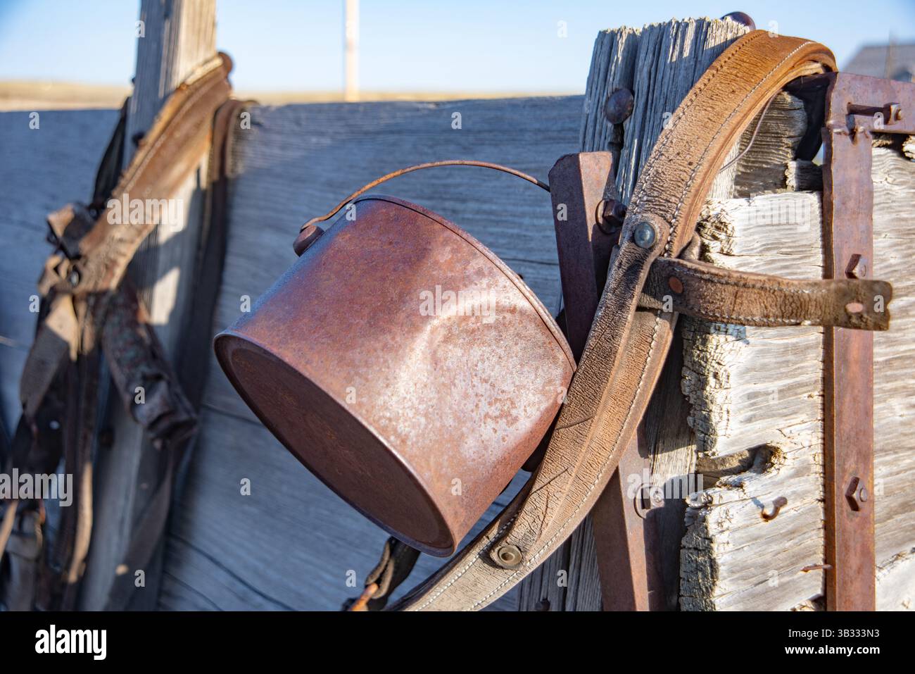 Rustikaler Metalleimer hängt an einem abgenutzten Holzbuckboard-Wagen auf einer Ranch in Western Wyoming während der goldenen Stunde Stockfoto