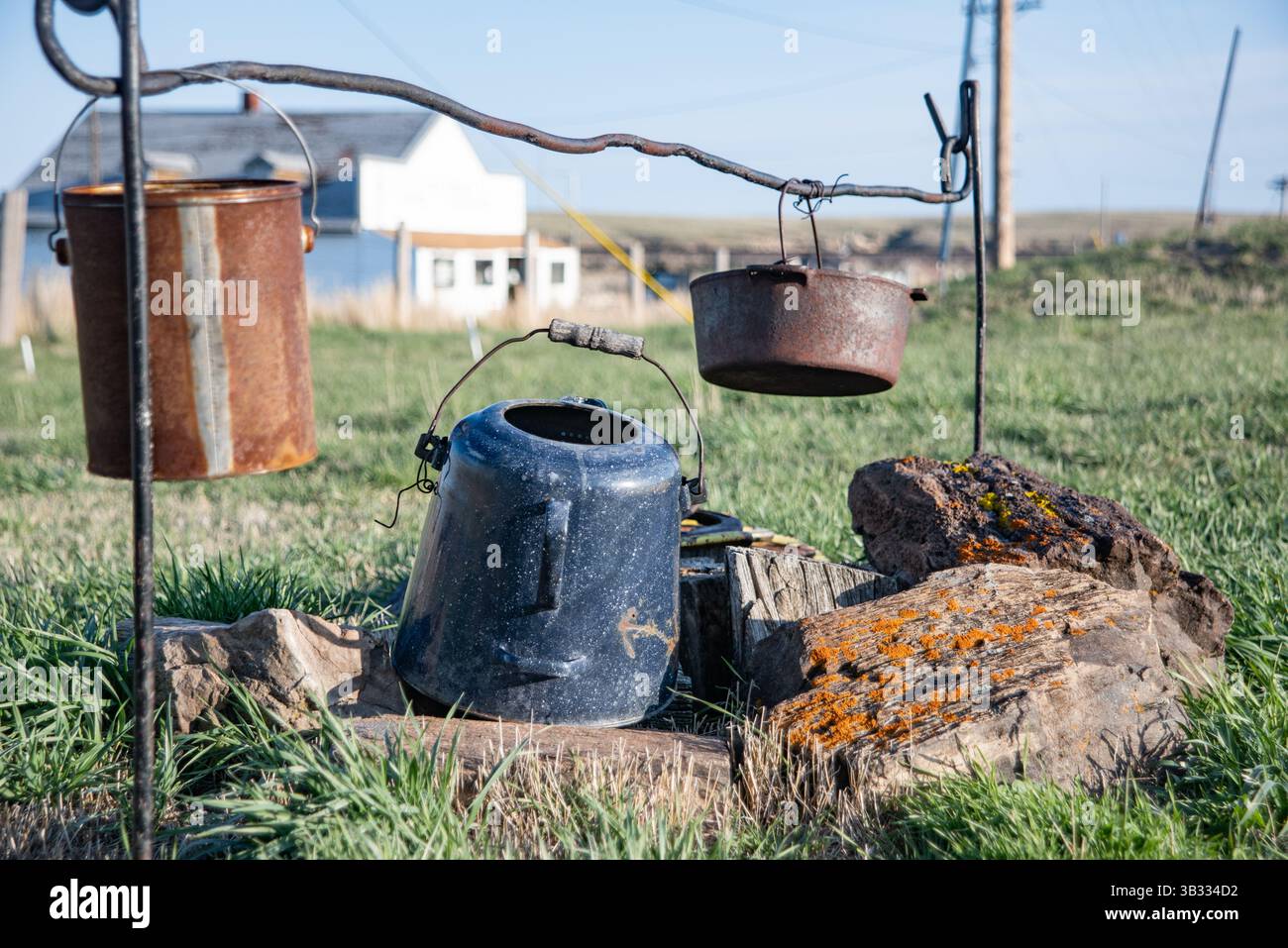 Ein Cowboy-Lagerfeuer mit einem alten Wasserkocher, zwei Töpfen, die an einem Metallrahmen auf der ländlichen Western Wyoming Ranch hängen, und ein verlassenes Gebäude. Stockfoto