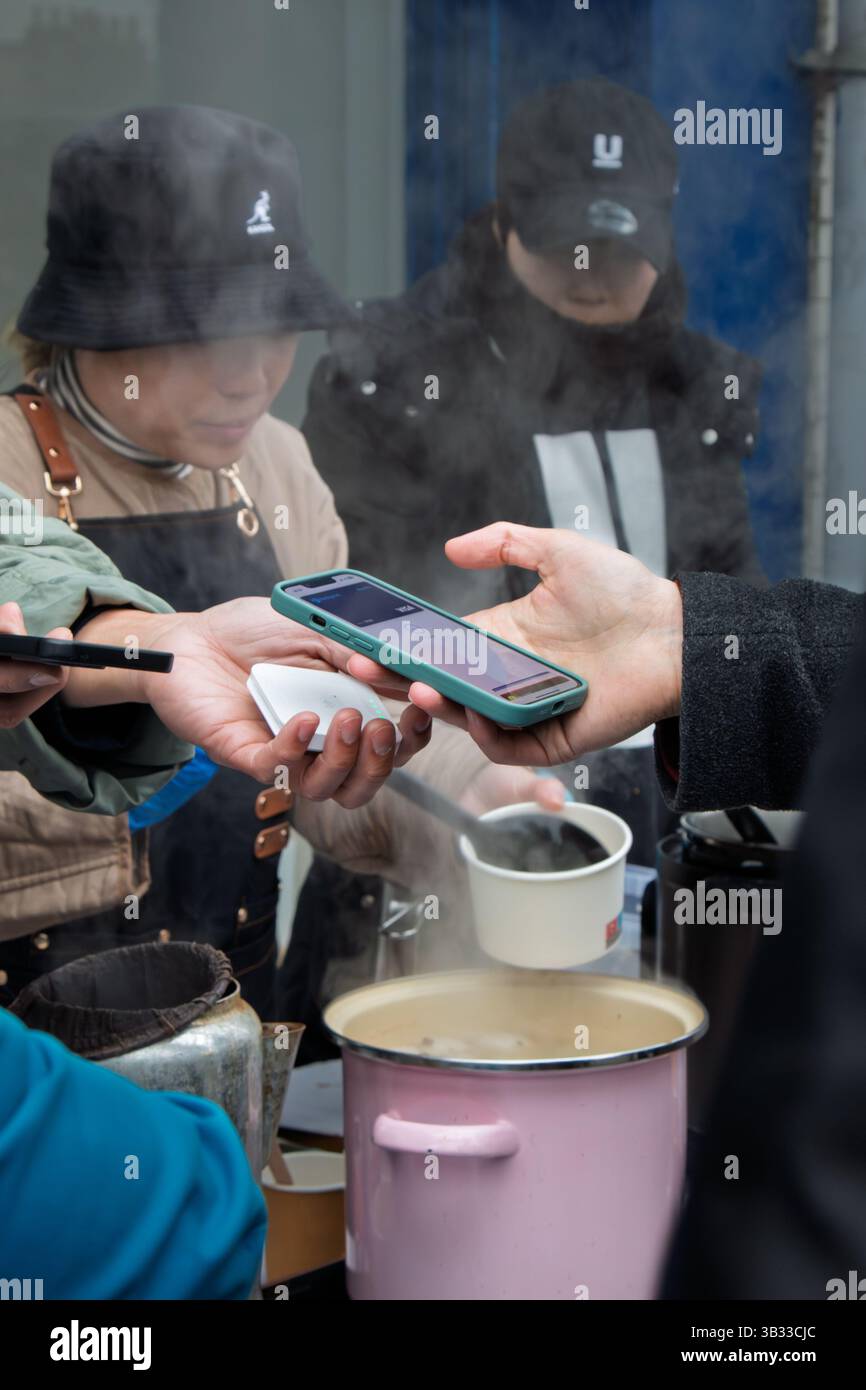 Ein Kunde verwendet sein Mobiltelefon, um an einem Imbissstand auf der Mill Road Winter Fair in Cambridge, England, Großbritannien zu bezahlen Stockfoto