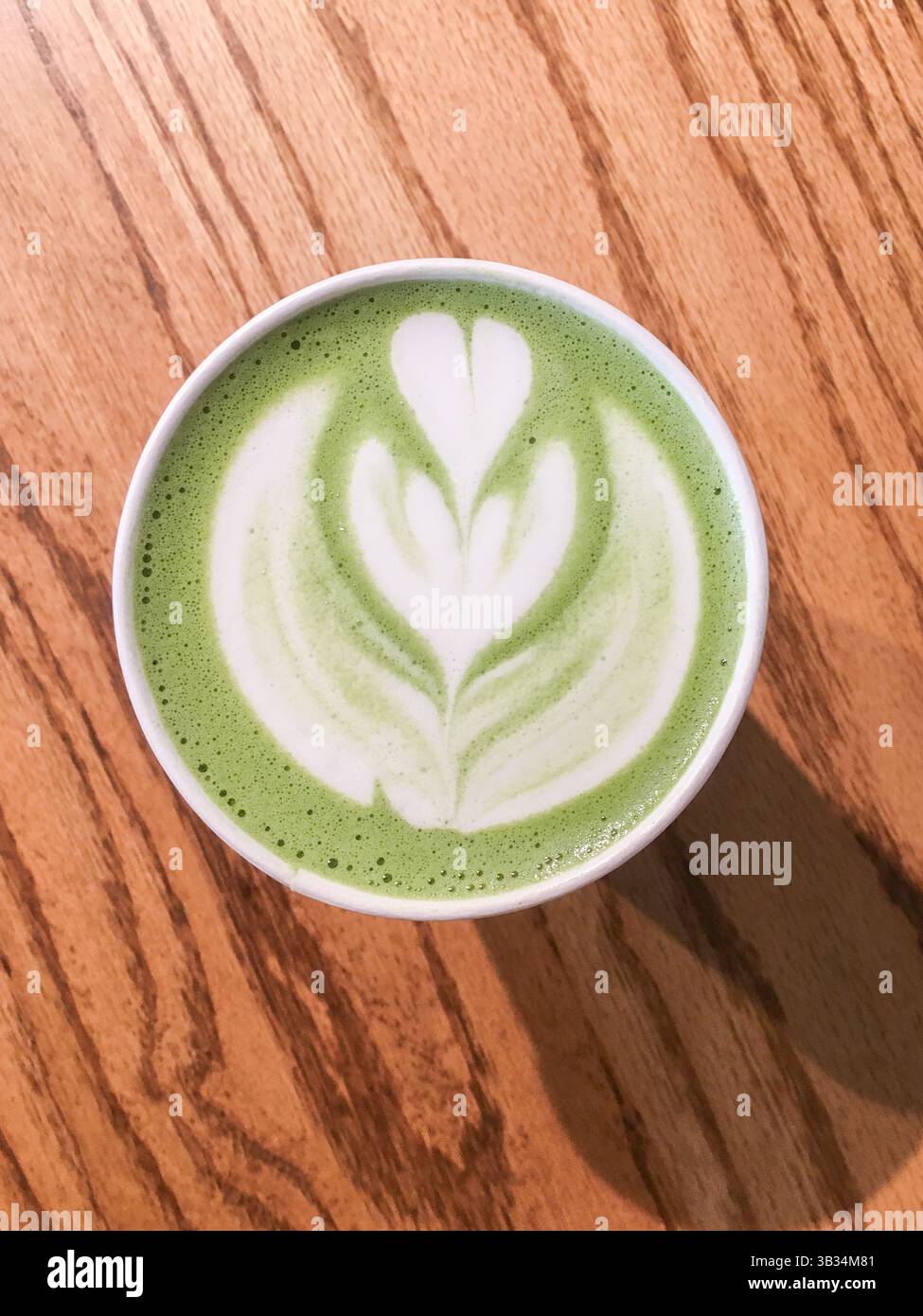 Blick von oben auf eine Tasse Matcha Latte mit schönen grünen und weißen Latte Art auf einem Holztisch, perfekt für Themen von gesunden Getränken, Café Kultur, gemütlich Stockfoto
