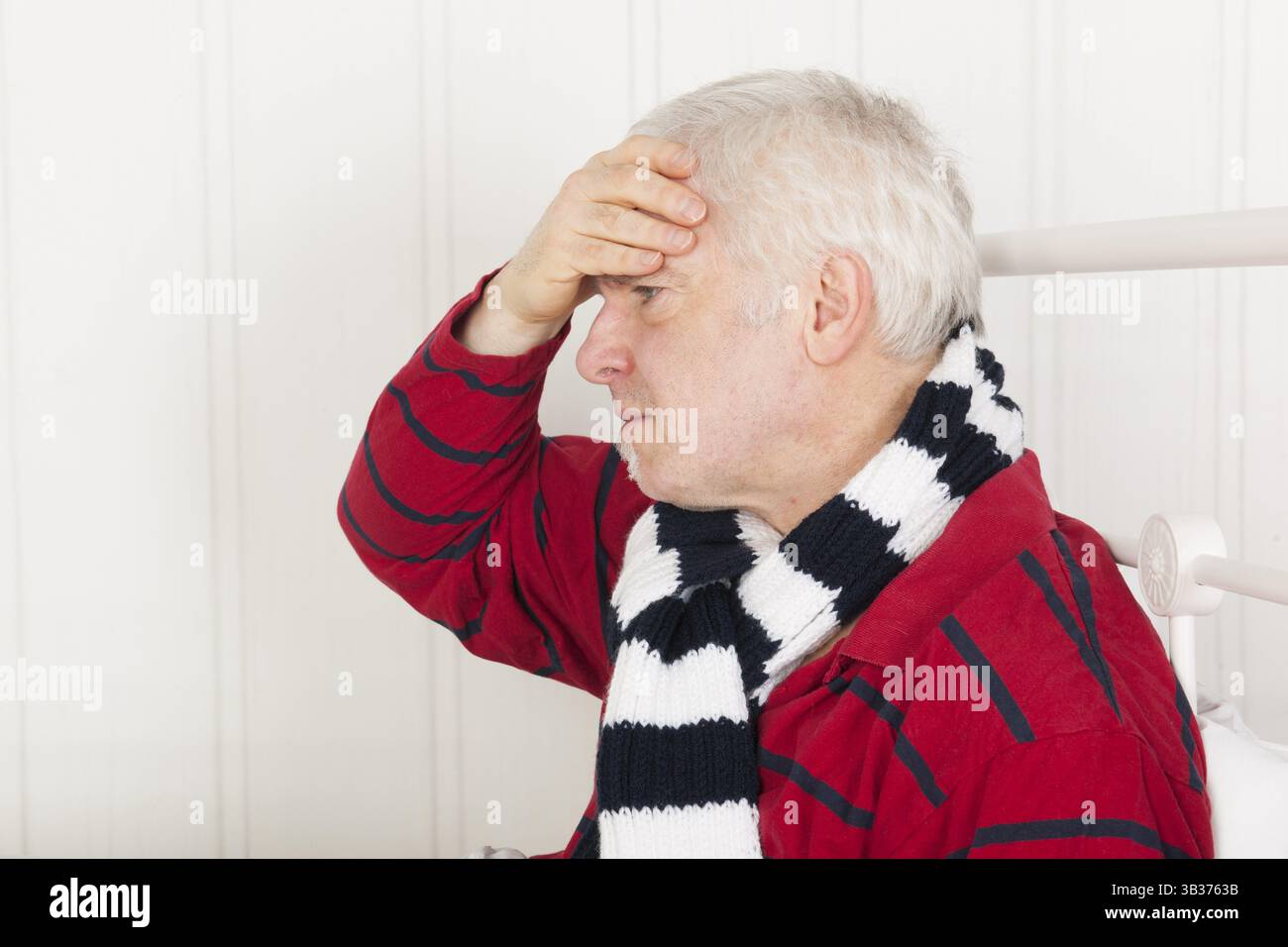 Älterer kranker Mann sitzt im Bett mit Eiskissen gegen Kopfschmerzen Stockfoto