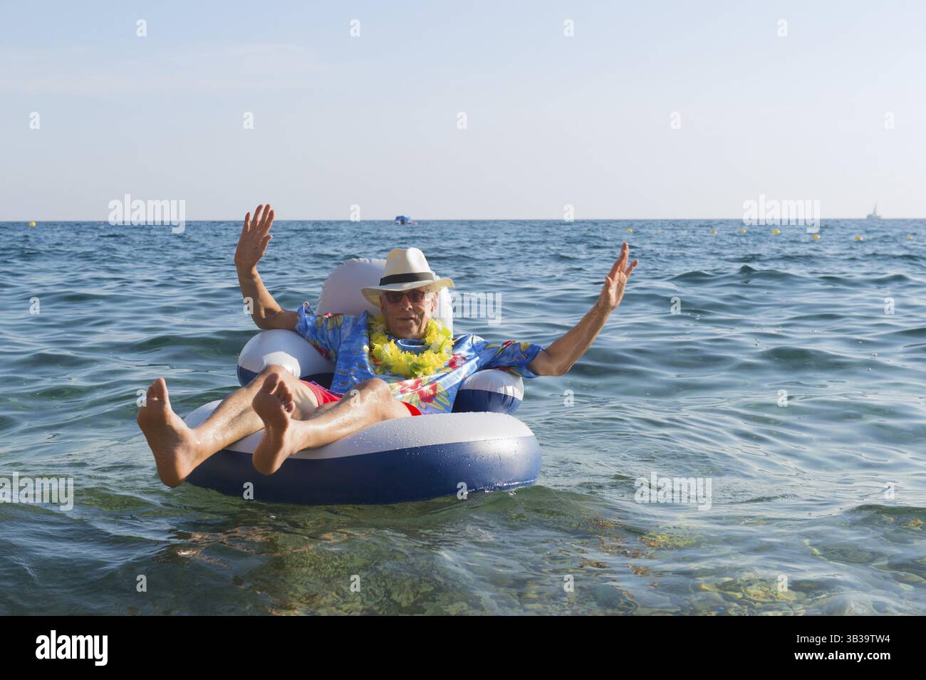 Senior woman mit Hawaii-Hemd und Blumen schweben am Meer Stockfoto