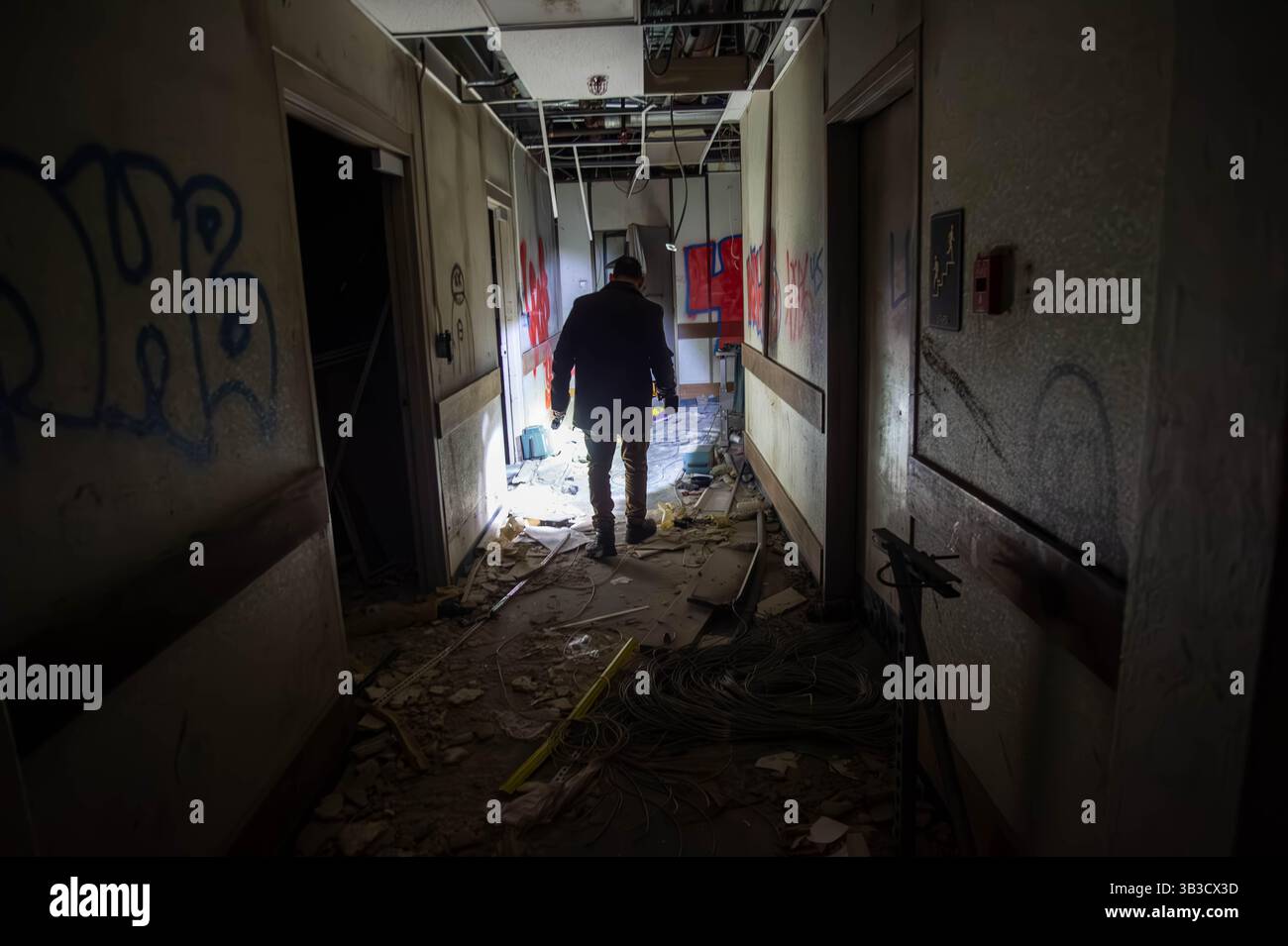 Dunkler verlassener Flur mit roten Totenkopfgraffiti und einer geheimnisvollen Silhouettenfigur, ideal für gruselige, unheimliche, urbane Entdeckungen und Horrorthemen. Stockfoto
