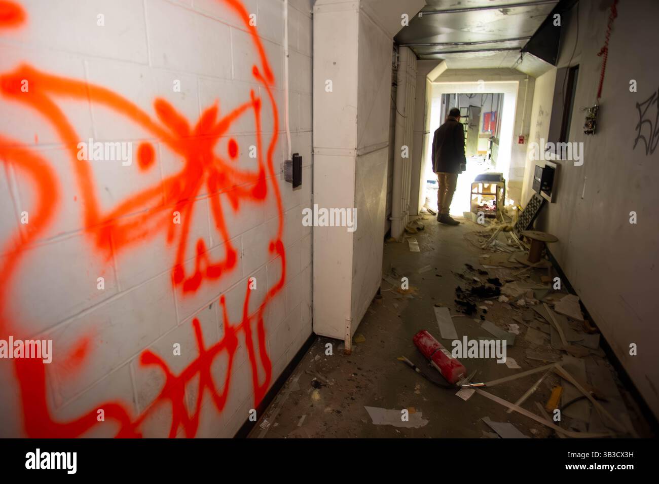 Dunkler verlassener Flur mit roten Totenkopfgraffiti und einer geheimnisvollen Silhouettenfigur, ideal für gruselige, unheimliche, urbane Entdeckungen und Horrorthemen. Stockfoto