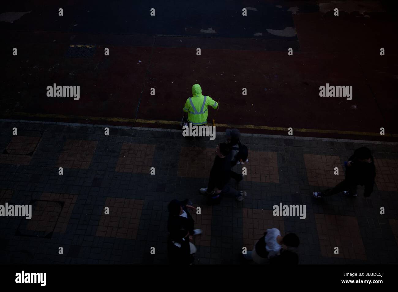 Straßenreiniger in Neon steht allein auf einer dunklen, leeren Strecke, während die Menge hinter ihm verblasst Stockfoto