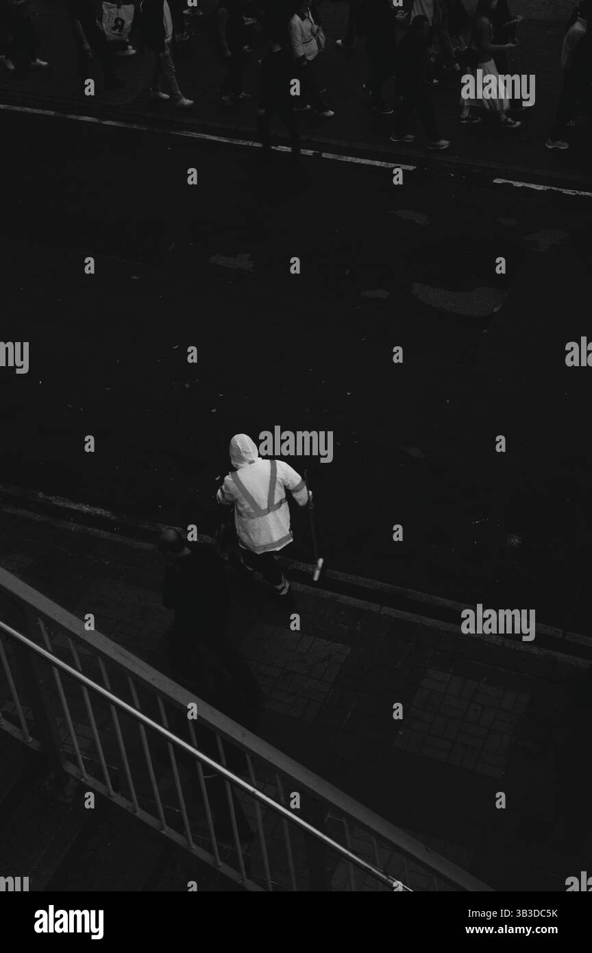 Straßenreiniger in reflektierender Ausrüstung arbeitet leise unter der Menge in einer schwarz-weißen Stadt Stockfoto