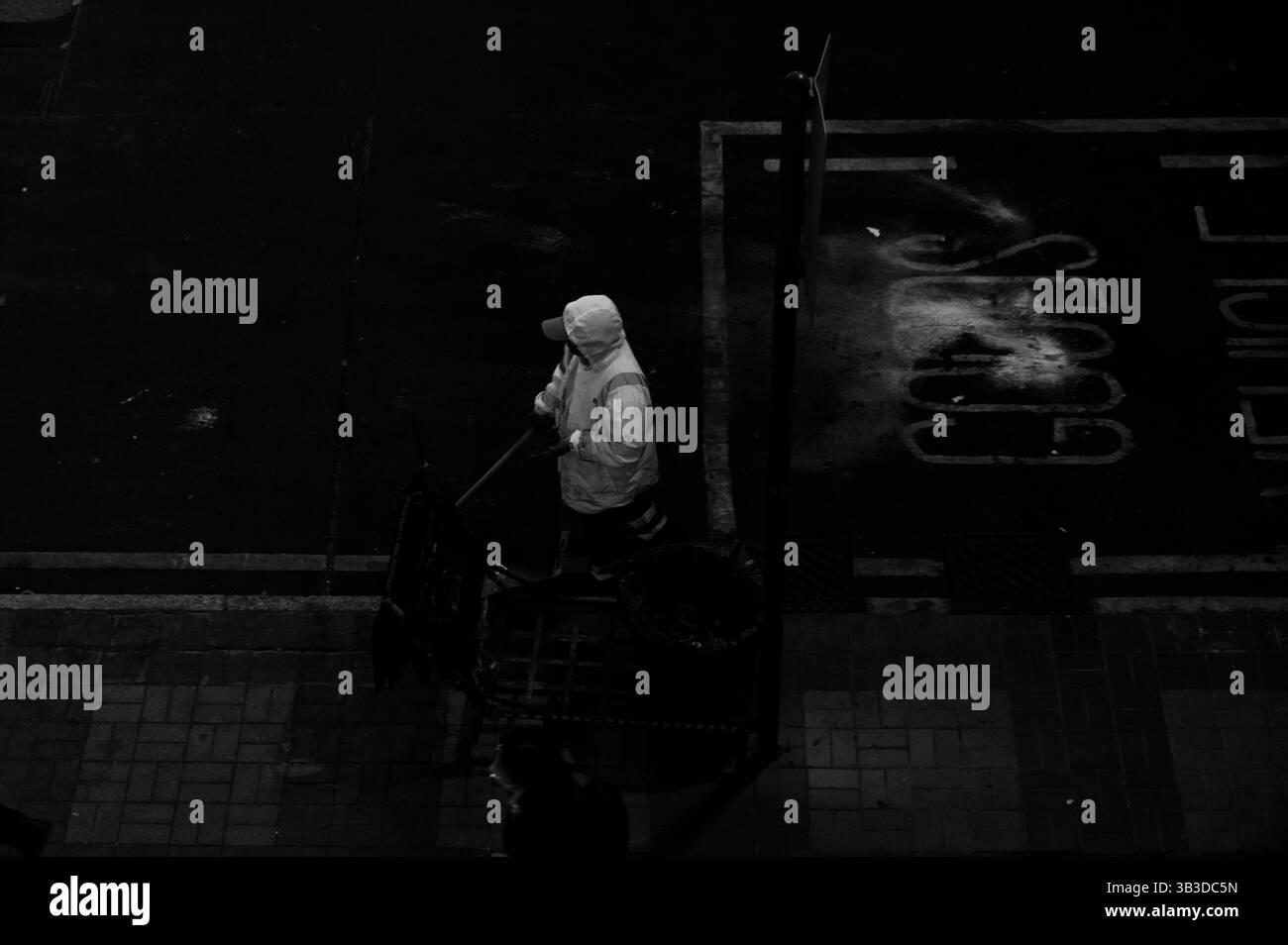 Einsamer Straßenreiniger bewegt sich durch die Schatten in einem ruhigen Stadtmoment, das in Schwarz-weiß festgehalten wird Stockfoto