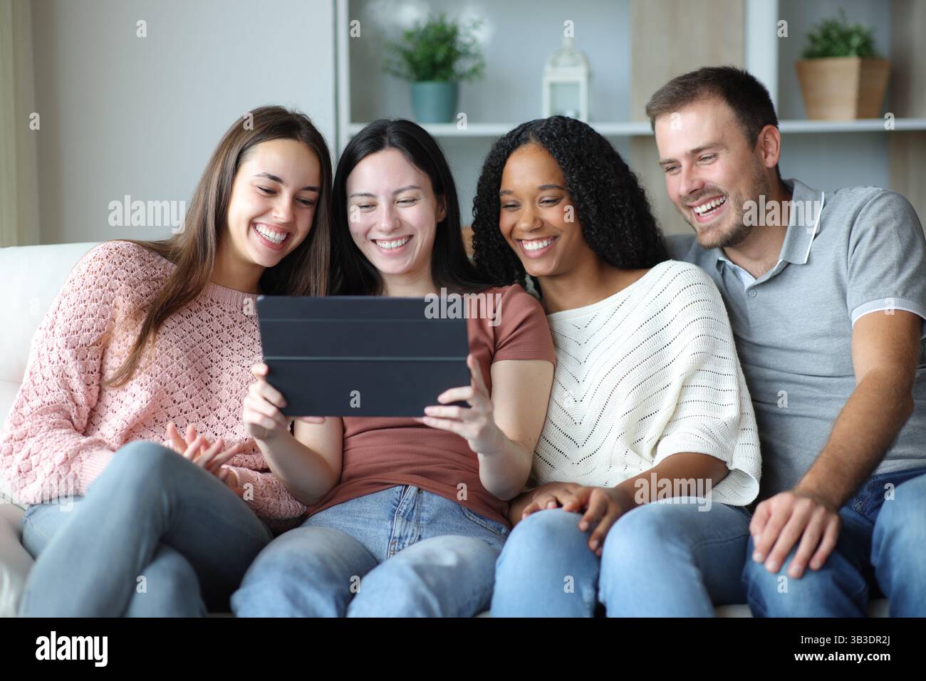 Glückliche interrassische Gruppe von Freunden, die zu Hause auf einer Couch sitzen Stockfoto