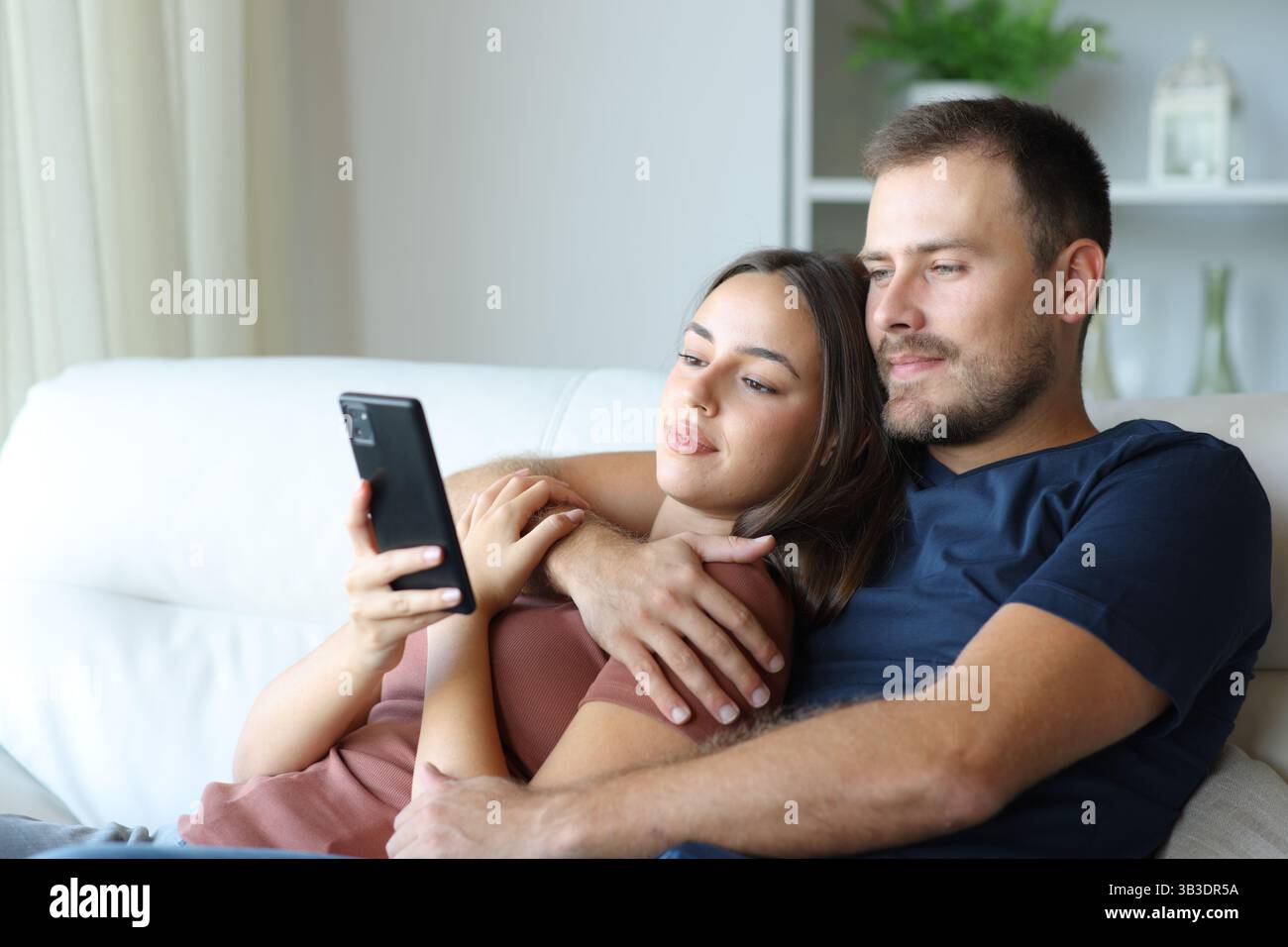 Entspanntes Paar, das zu Hause auf einer Couch auf dem Handy sitzt Stockfoto