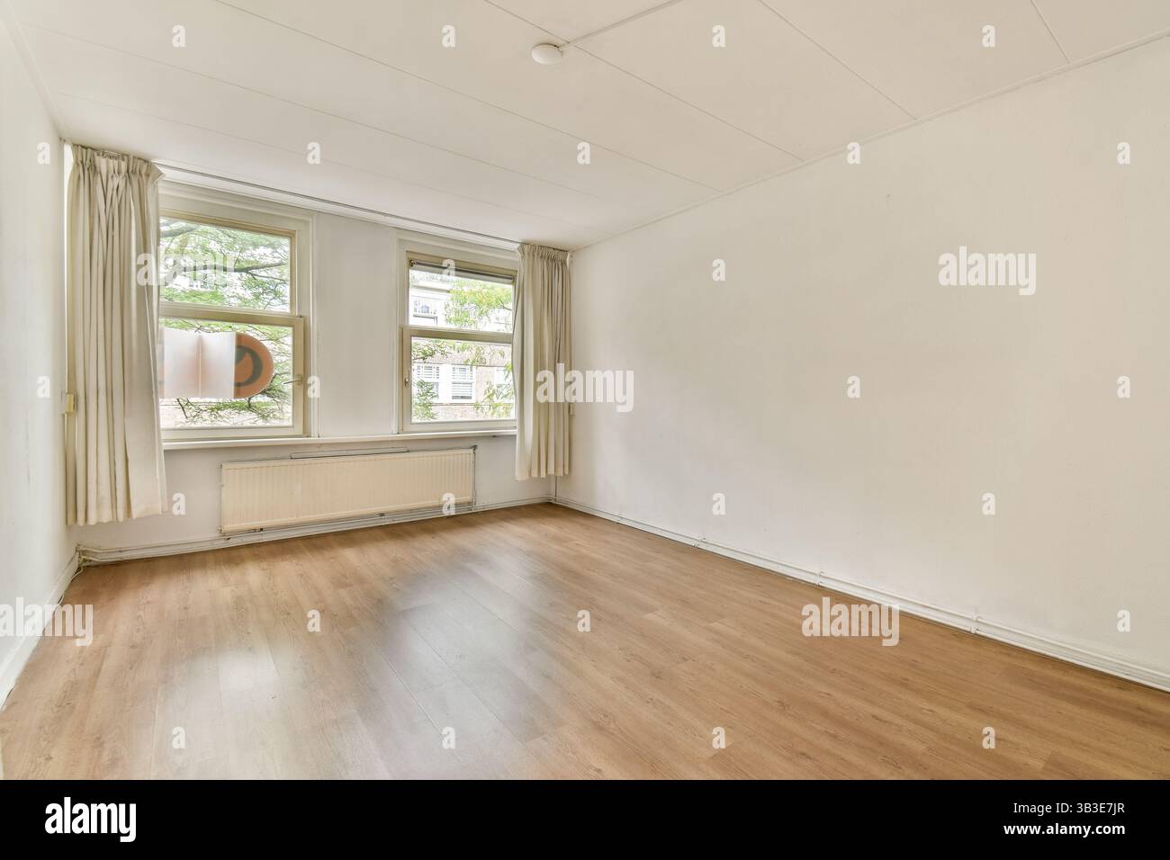 Ein geräumiger, sonnendurchfluteter Raum mit großen Fenstern und Wänden in neutralen Farben. Das schlichte Design betont eine minimalistische Ästhetik. Perfekt für modernes Wohnen. Stockfoto