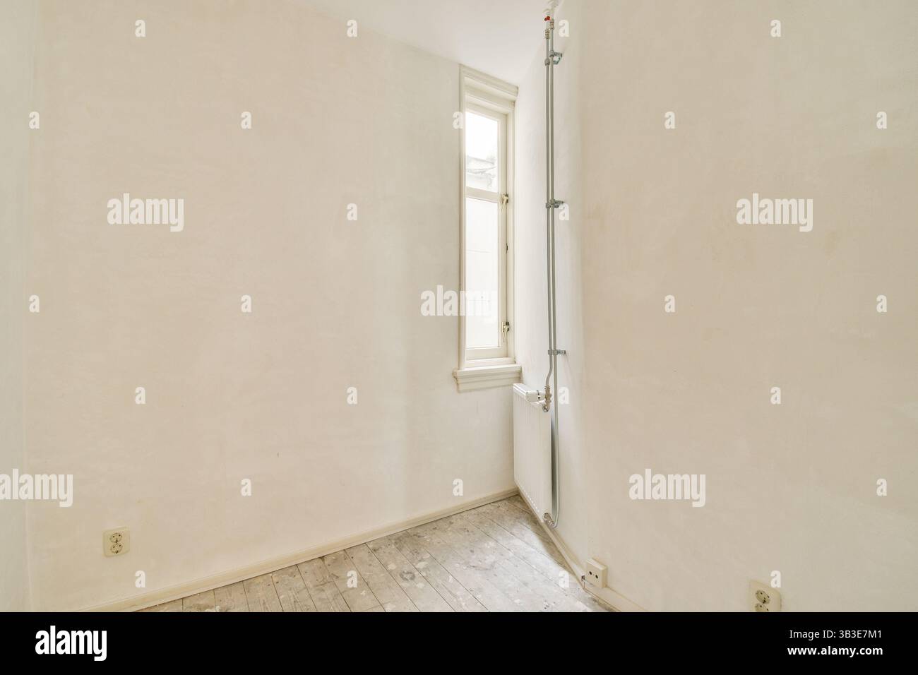 Ein leerer Raum mit minimalistisch weißen Wänden und einem einzigen Fenster, durch das Tageslicht den Raum beleuchtet. Der Boden ist einfach und unauffällig. Stockfoto
