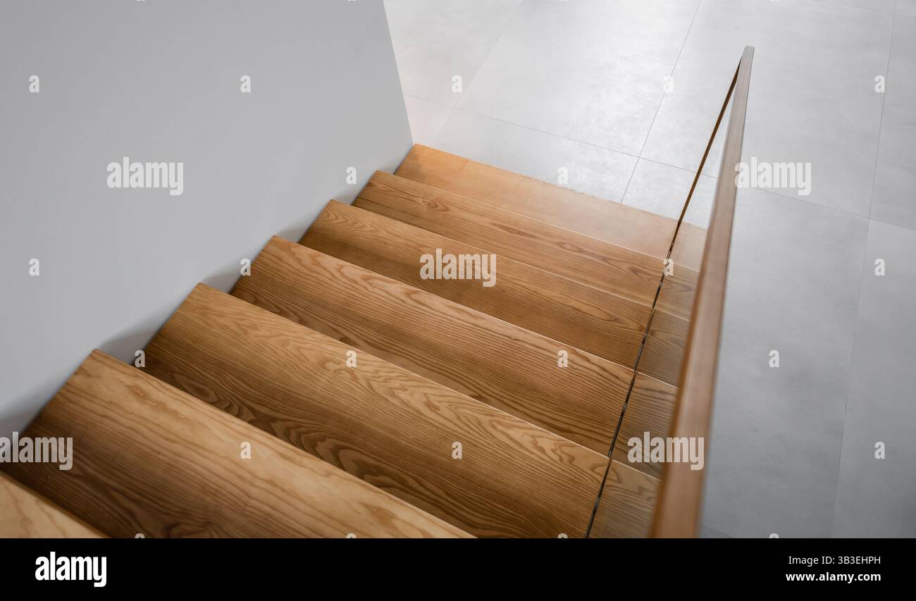Holztreppe in einem Gebäude. Leere Treppe nach unten mit weißen Wänden. Foto von sieben Holzstufen in warmen Tönen. Stockfoto