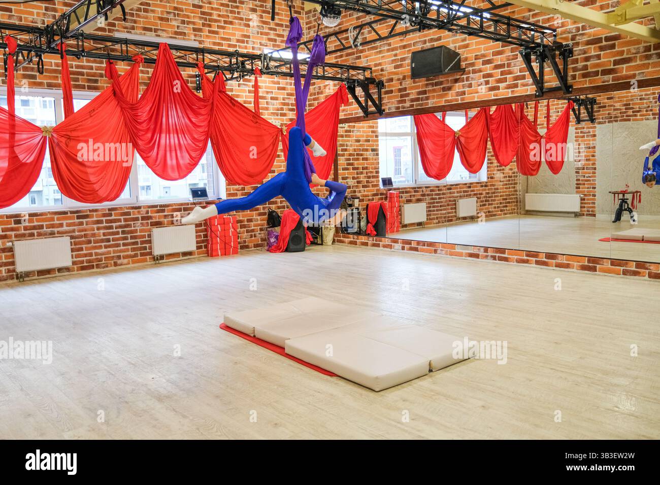 Moskau, Russland, 30.11.2024 Eine Frau führt einen Handstand auf einer Matte in einem Fitnessstudio auf. Der Fitnessraum ist mit roten und weißen Vorhängen dekoriert und hat einen Spiegel auf dem T Stockfoto