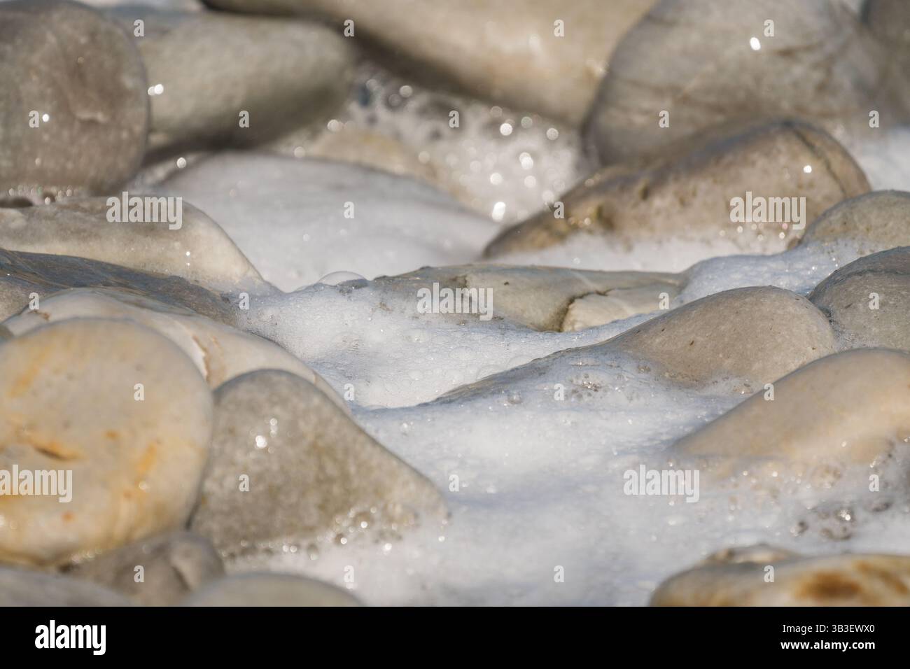 Felsen, Steine, Kieselsteine aus der Nähe, glänzend und nass umgeben von Meerwasser und Schaumkonzept abstrakte Natur Hintergrund, Hintergrund, Tapete Stockfoto