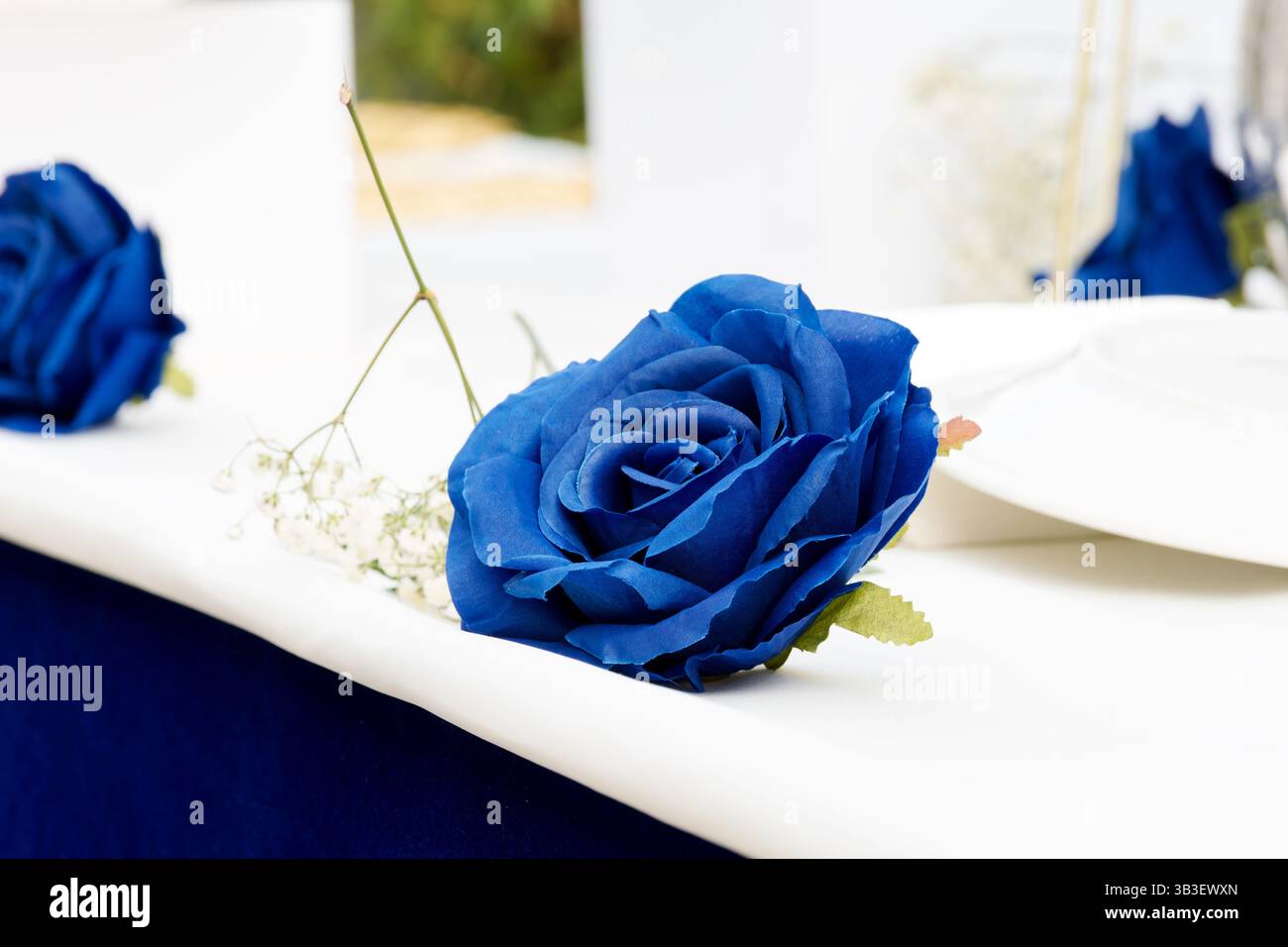 Handgefertigte blaue Papierrose, die als dekoratives Herzstück auf einem festlichen oder Hochzeitstisch platziert wird. Stockfoto