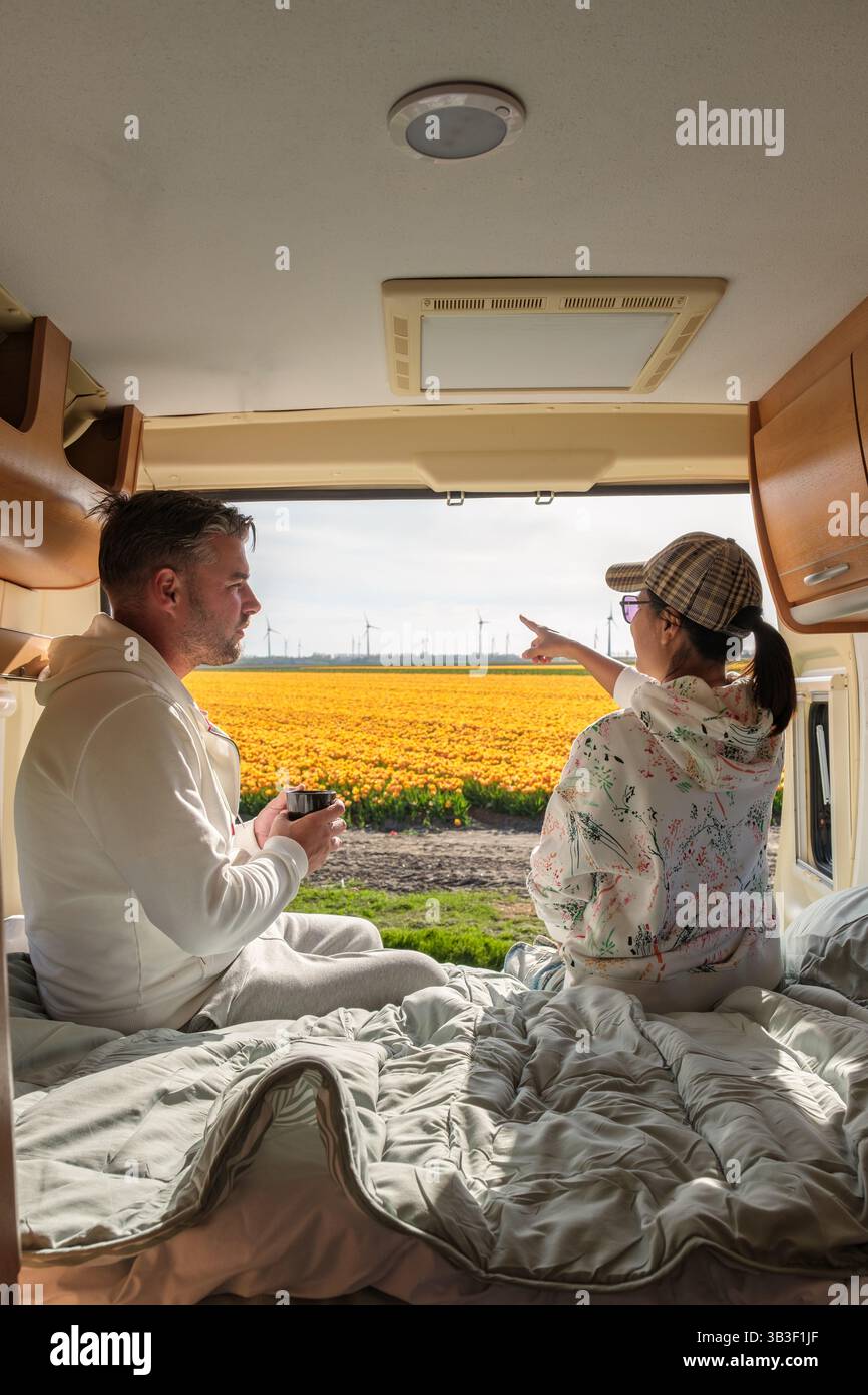 Ein Paar entspannt sich in einem Wohnmobil und blickt auf die lebhaften Tulpenfelder in Flevoland. Der Frühling bringt farbenfrohe Blüten und eine einladende Atmosphäre, perfekt für einen romantischen Kurzurlaub. Stockfoto